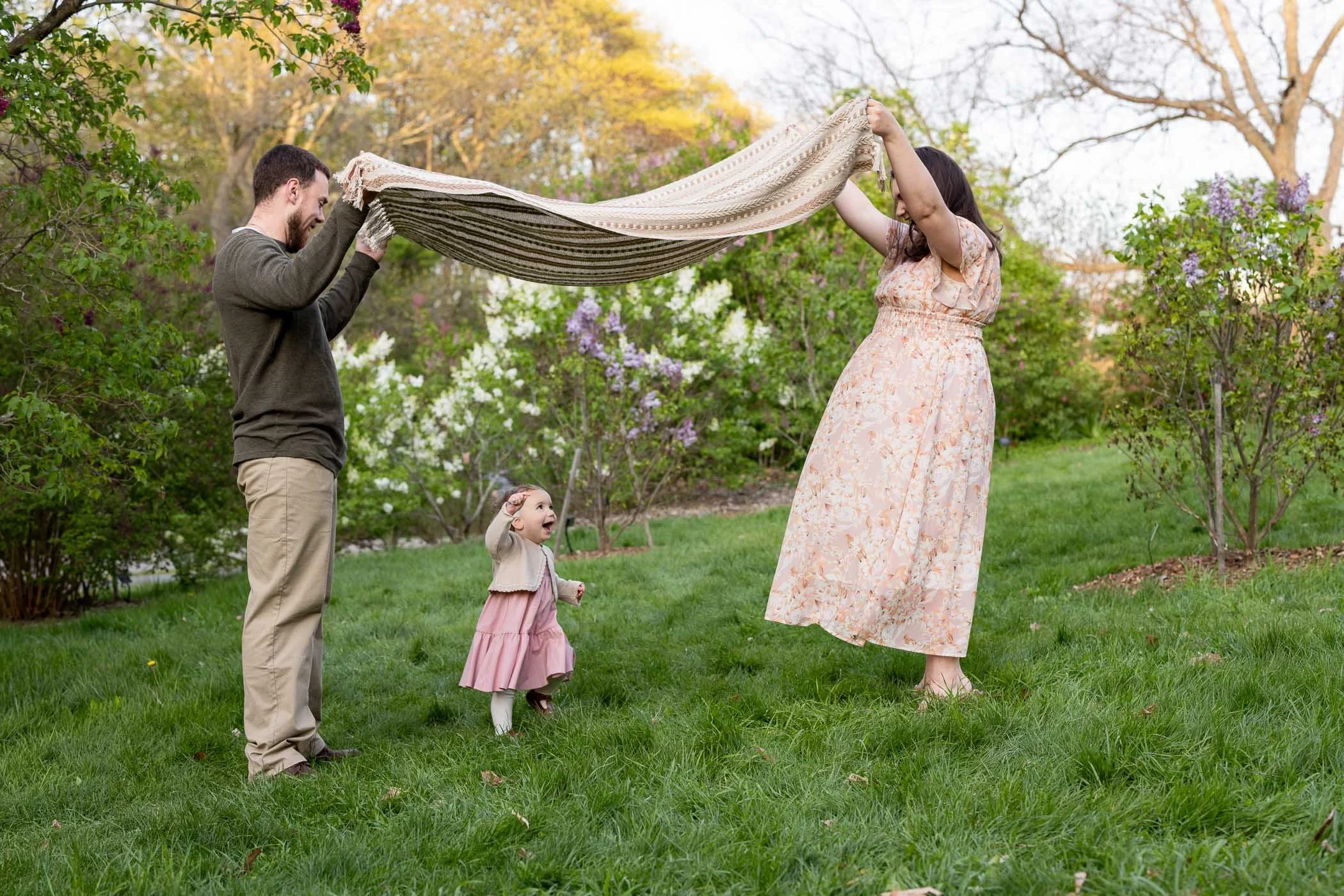 Little girl giggles while running under blanket being lifted by dad and mom