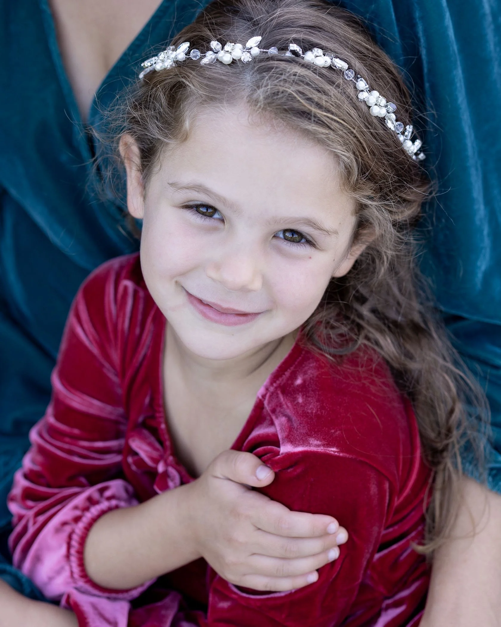Little girl wearing red dress sitting on moms lap has content expression