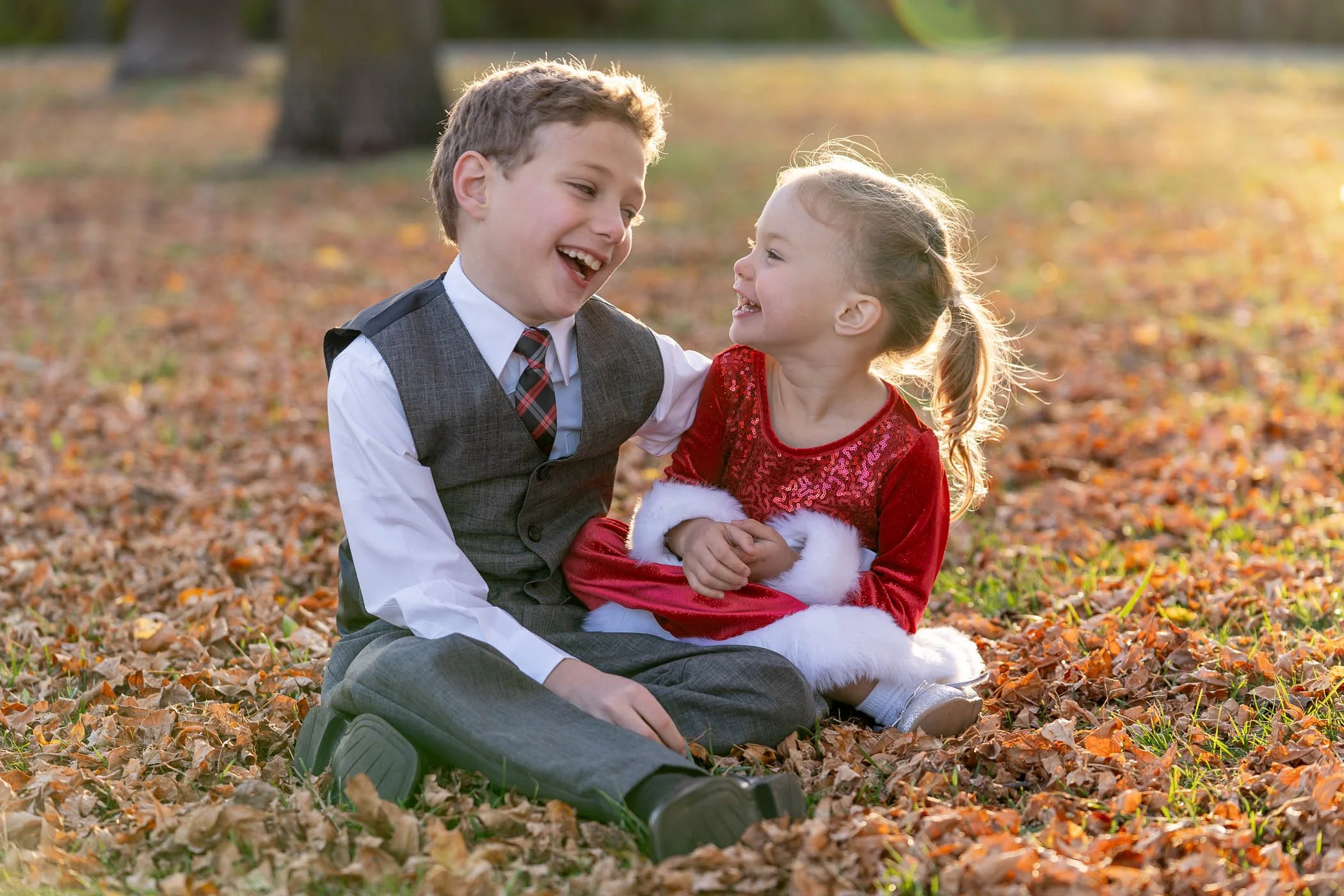 Young brother and sister sitting together giggling at each other surrounded by pretty fall colored leaves showing joy and happiness