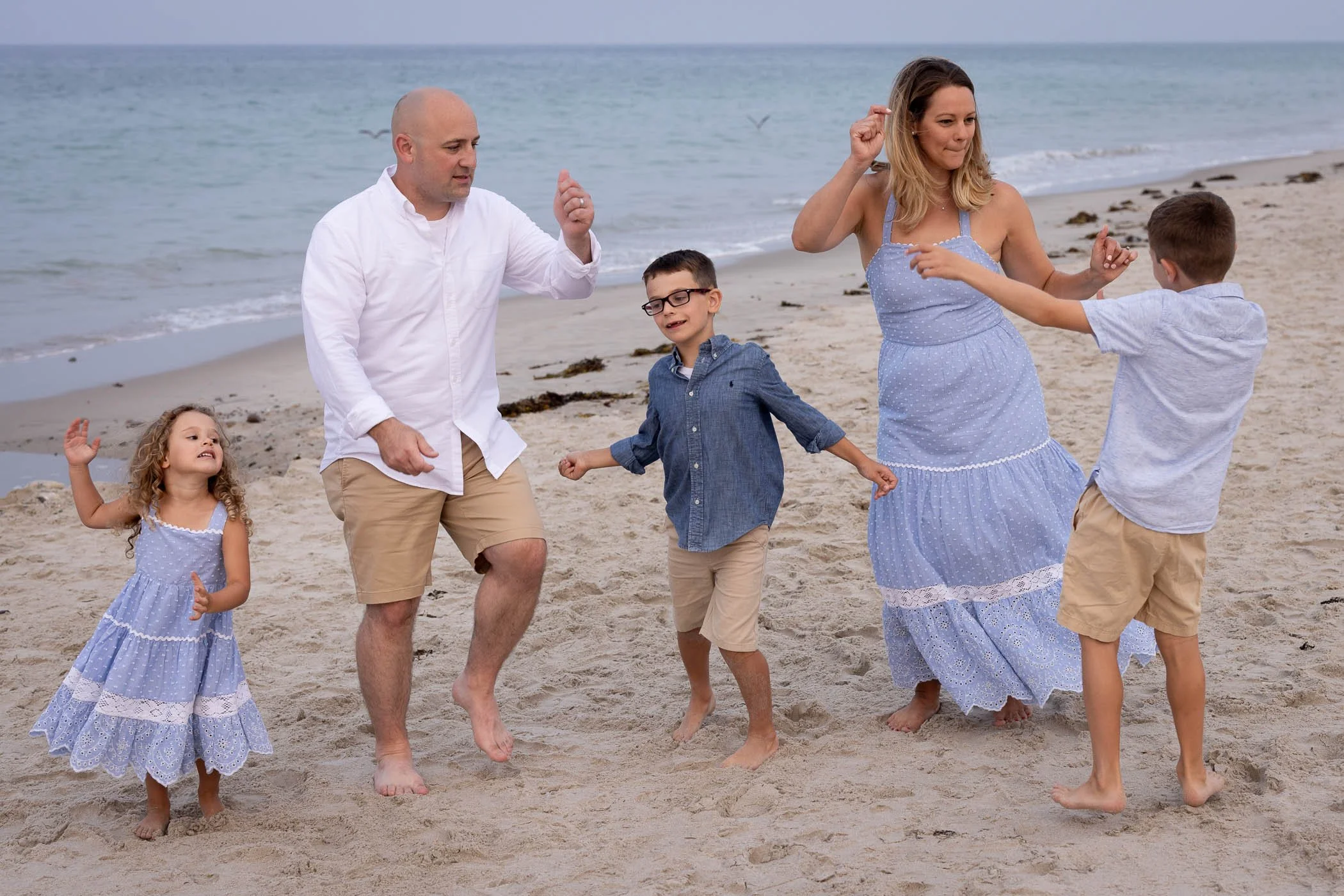 Family of five dance on the beach barefoot with ocean behind