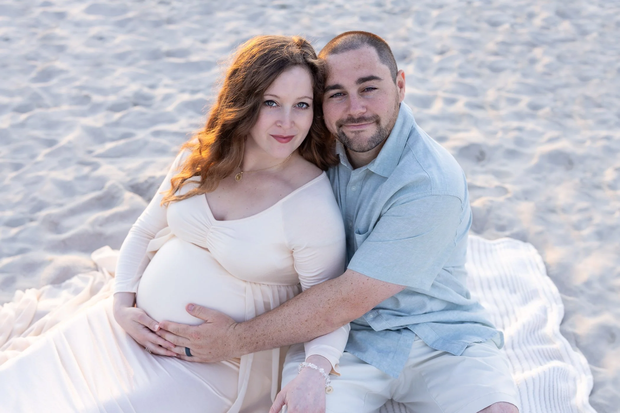 Dad hugging pregnant wife's belly while sitting on the beach