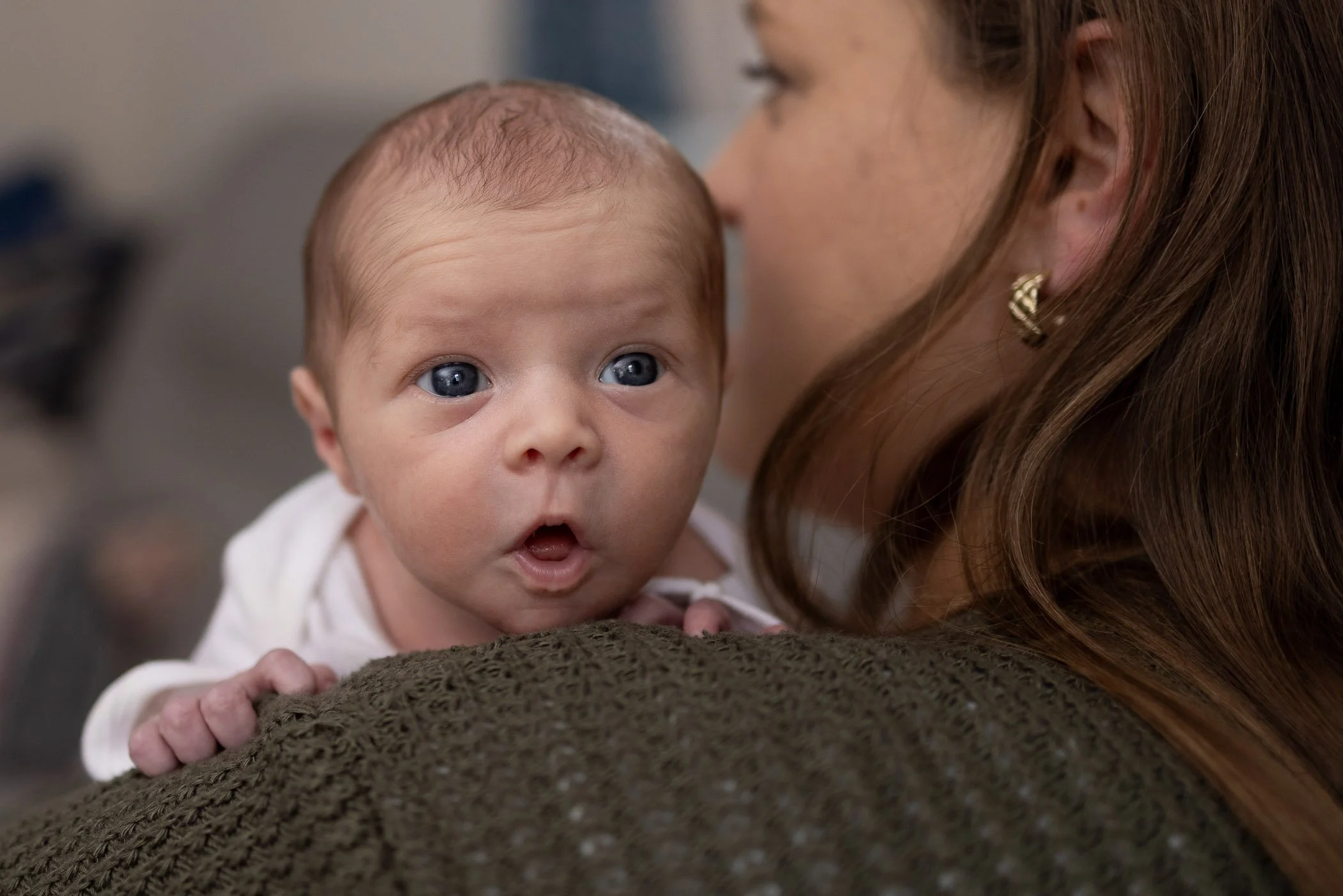 Newborn daughter looks over mom's shoulder with wide open eyes