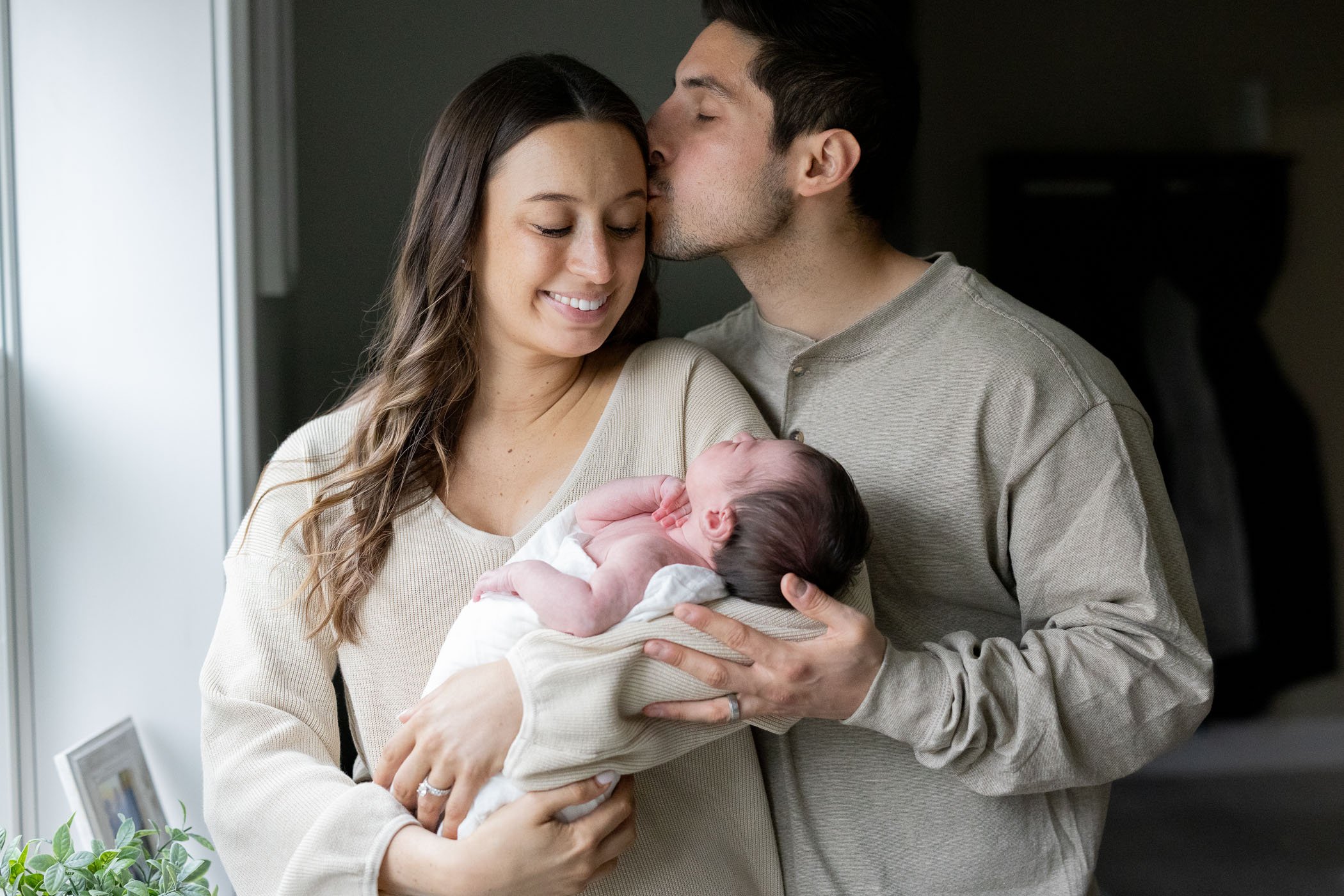 Mom cradling baby daugher while dad kisses mom