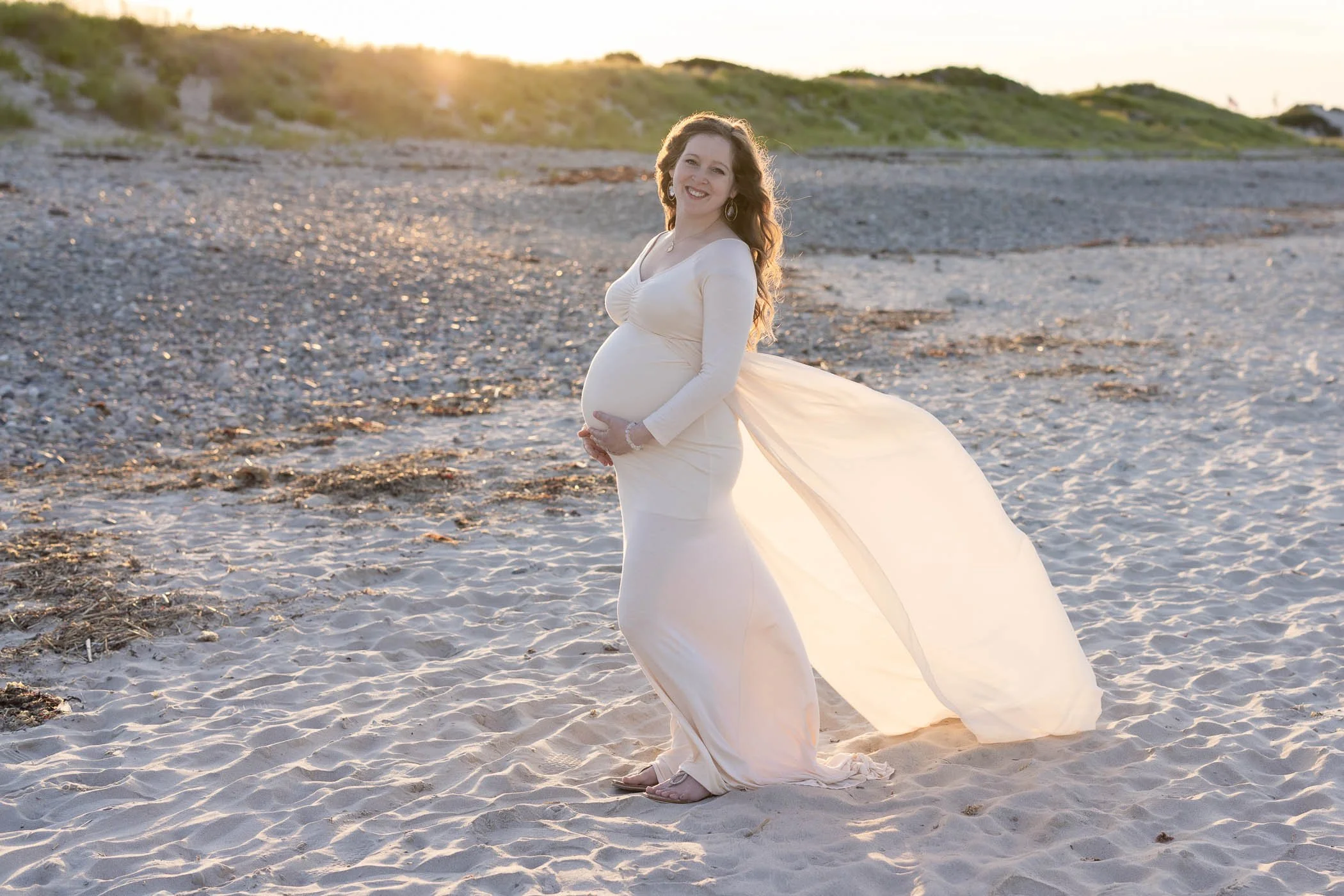 Radiant glow on pregnant woman standing on beach in long dress