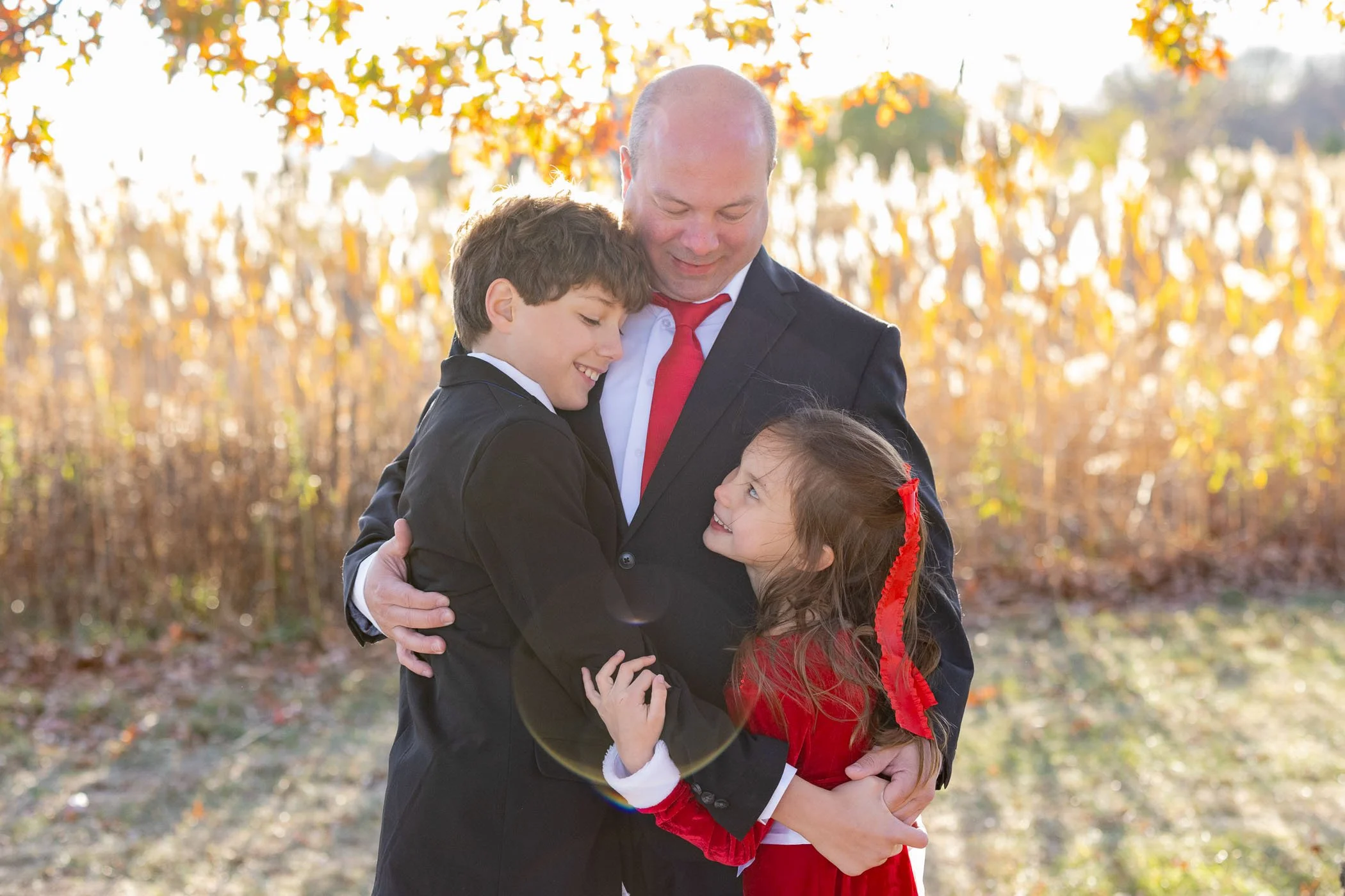 Dad son and younger daughter hugging and smiling at each other with glowy backlit sunlight showing love and connection
