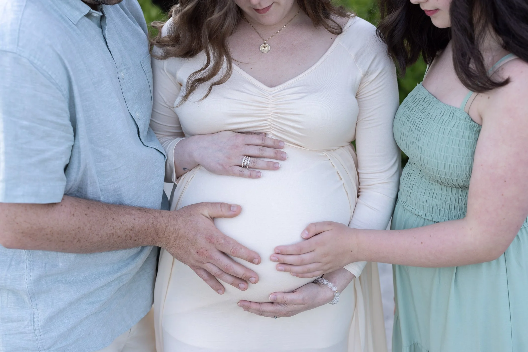 Several hands touch pregnant belly by family showing love