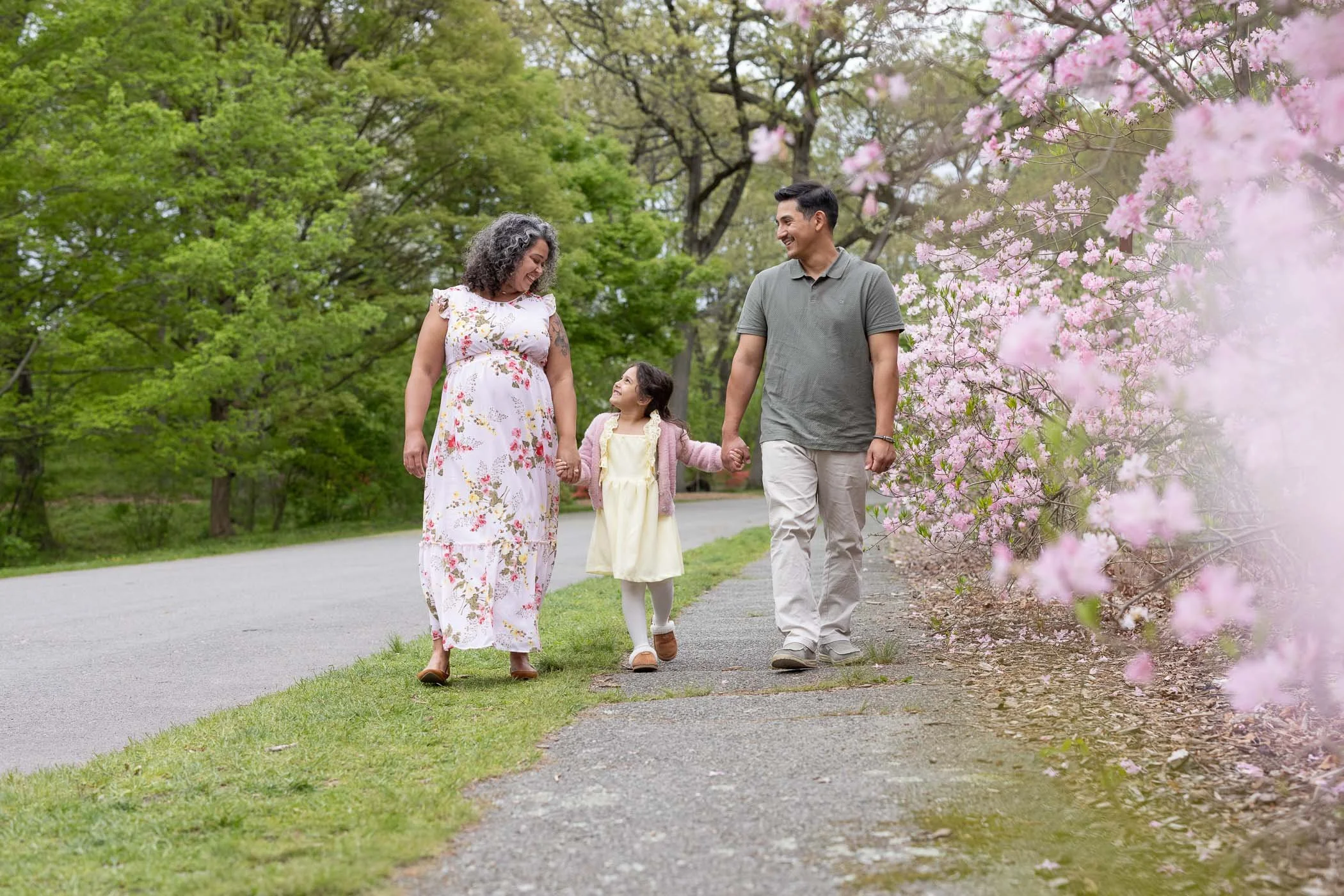 Mom dad and daughter walk next to pretty blooming pink flowers