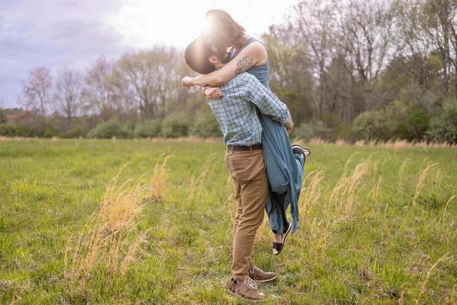 engaged man lifts woman while kissing in field