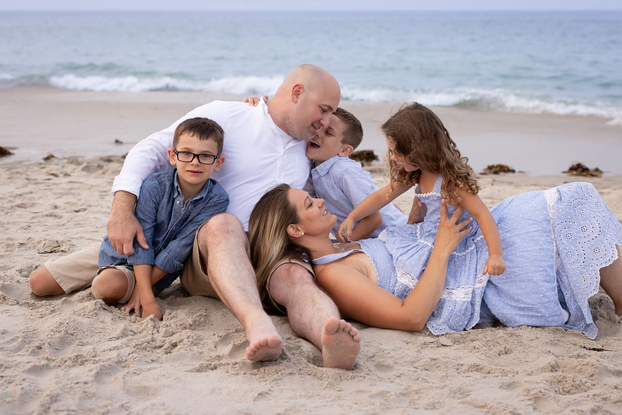 Family of five cuddle on beach showing love and connection.