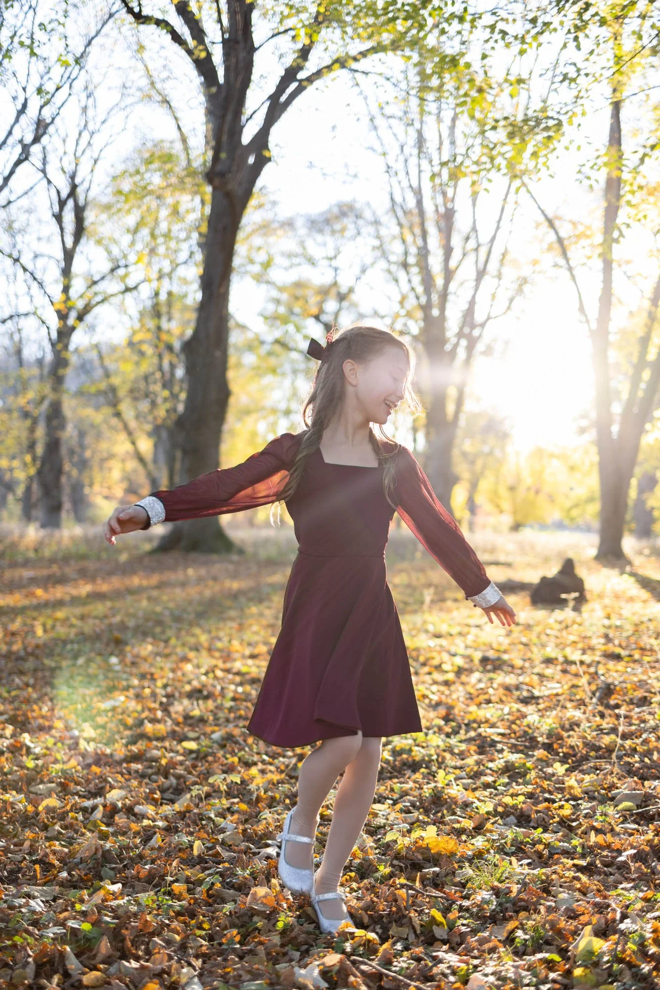 young girl twirling in the woods wearing maroon dress