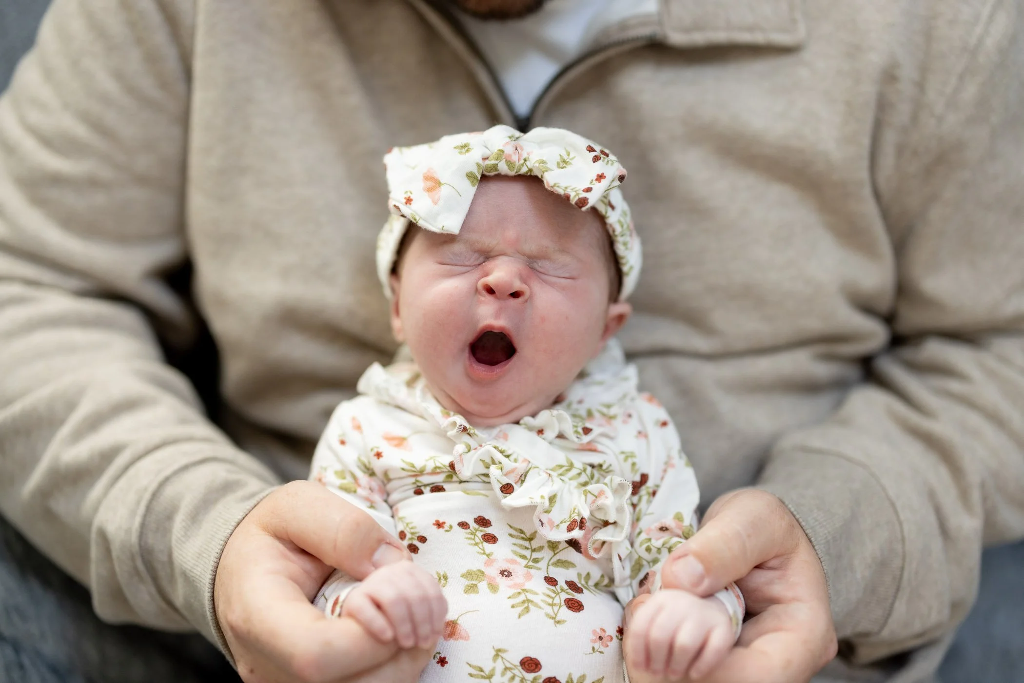 Infant girl yawning in daddy's lap while holding his fingers