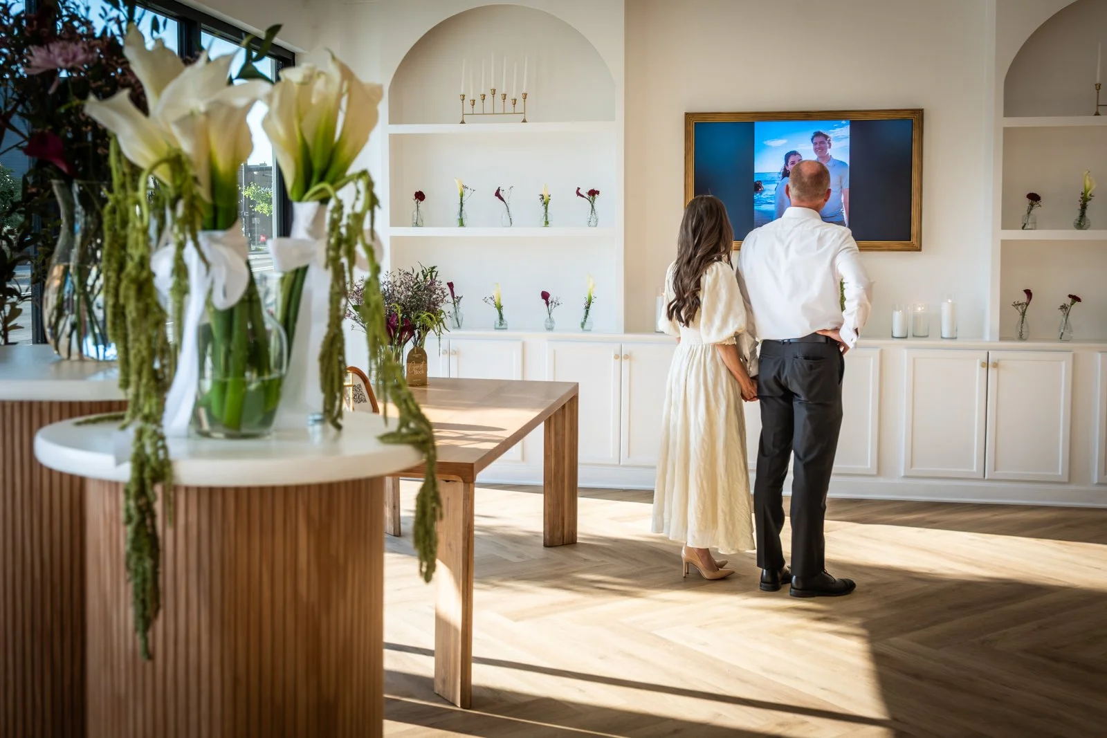Wedding couple standing inside La Fête in downtown Provo, with white floral arrangements and built-in bookcases