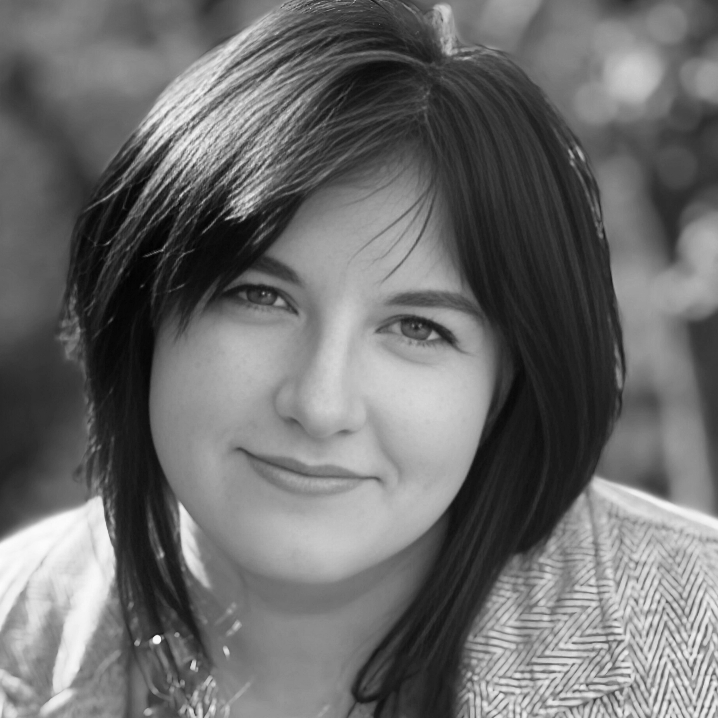 Black and white portrait of a woman with shoulder-length dark hair, smiling softly, outdoors with blurred background.
