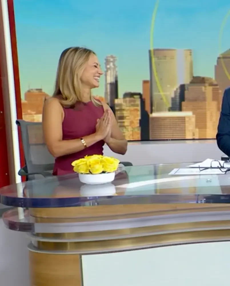 Katy sitting at a news desk with a cityscape backdrop.