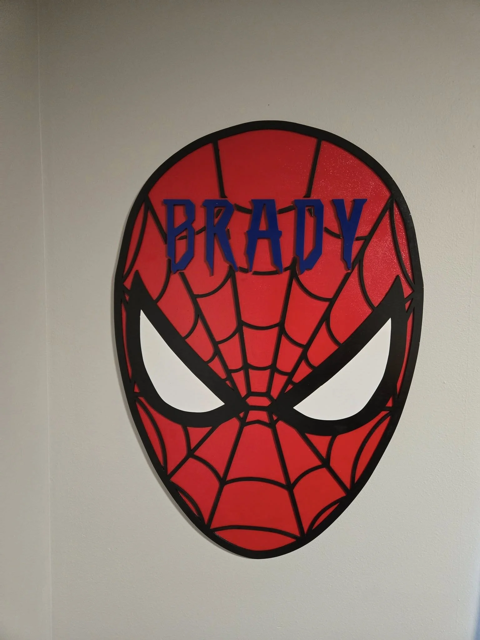 Red and black Spider-Man face mask wall decoration with the name 'Brady' in blue letters on a white wall.