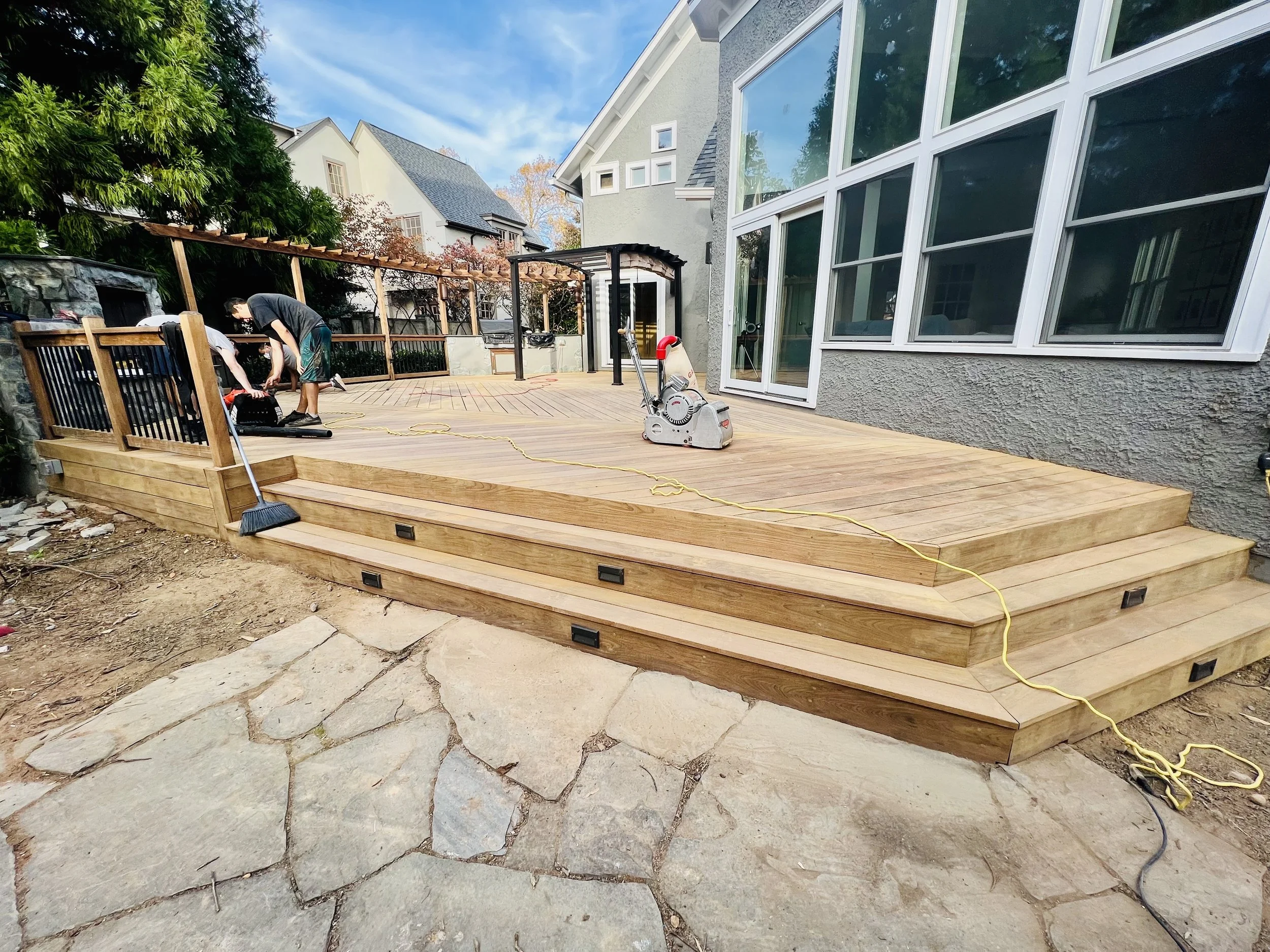 A newly constructed wooden deck with steps leading to a patio in backyard.