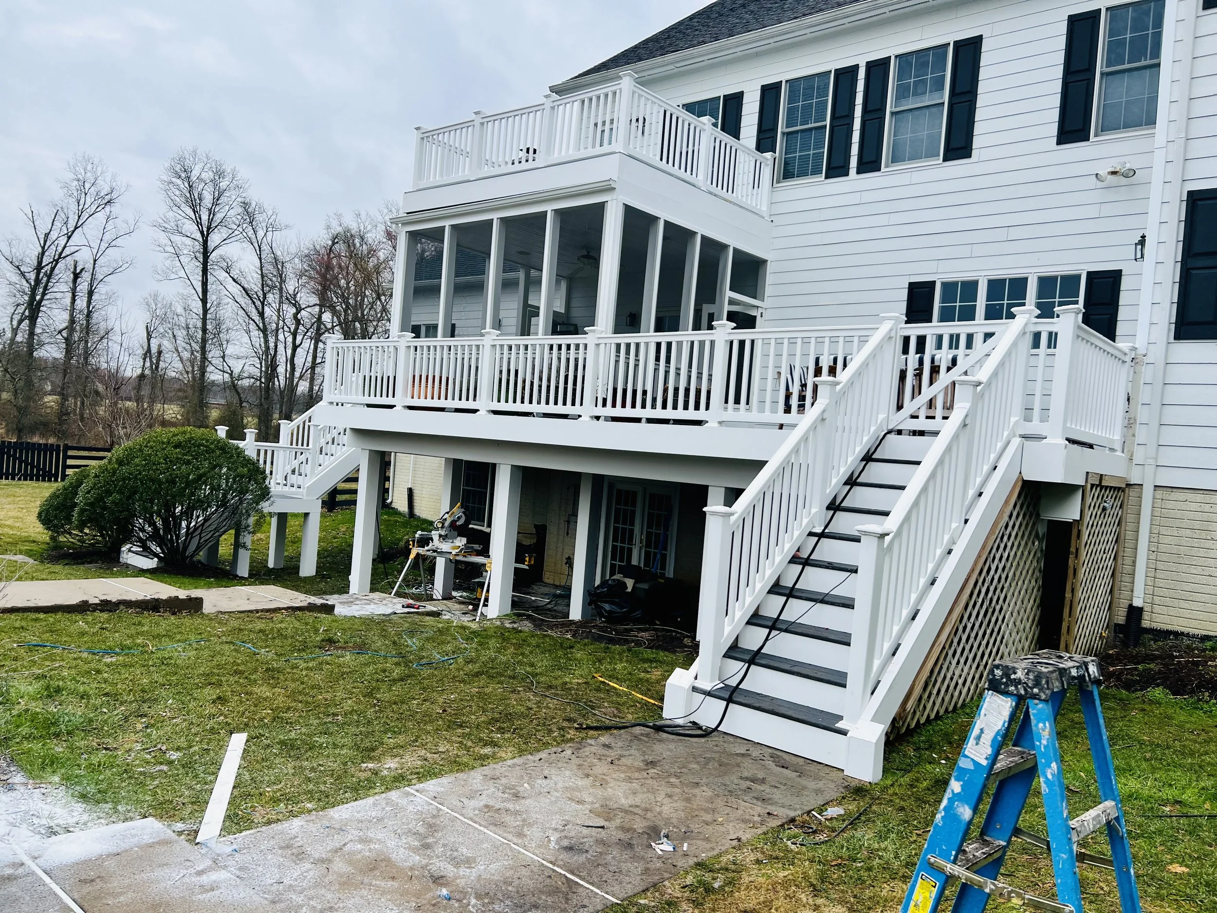 Newly built white multi-level wooden deck with stairs attached to the back of a house.