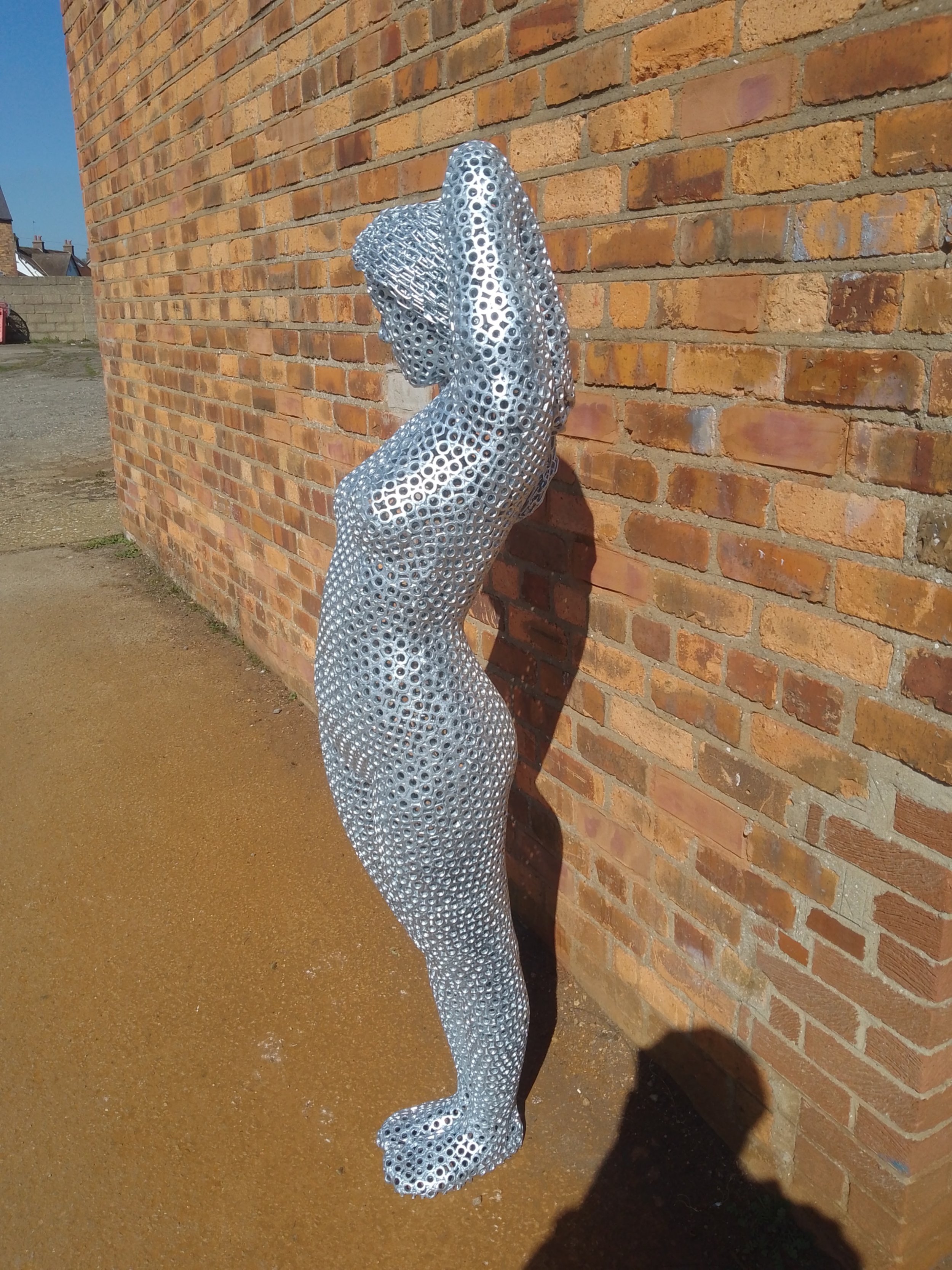 Woman-shaped sculpture in motion, welded from steel nuts with a matte silver finish. Appears to float, radiating strength and elegance.