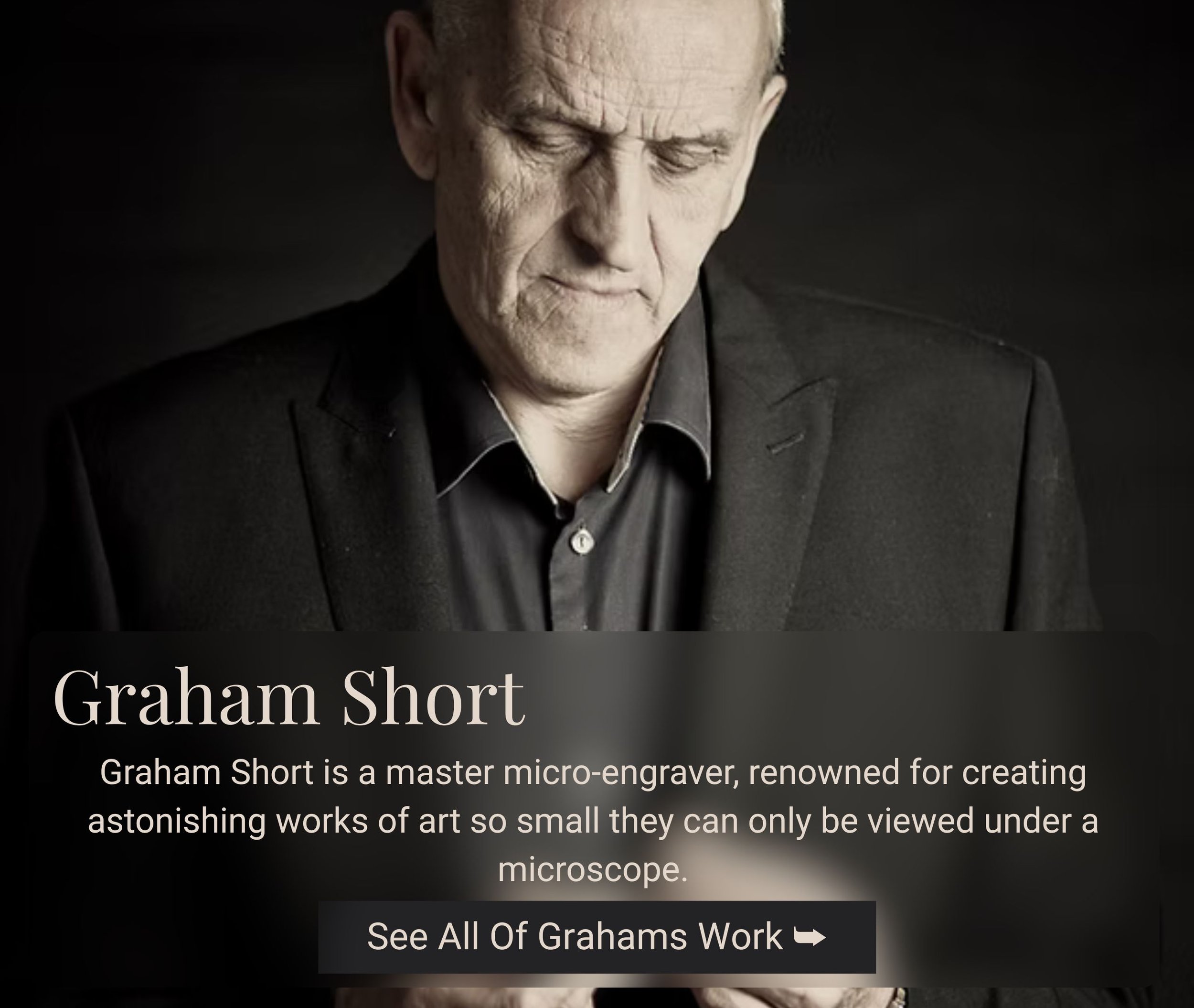 Portrait of Graham Short, a master micro-engraver, looking down with a serious expression, wearing a black suit and shirt, with a dark background.