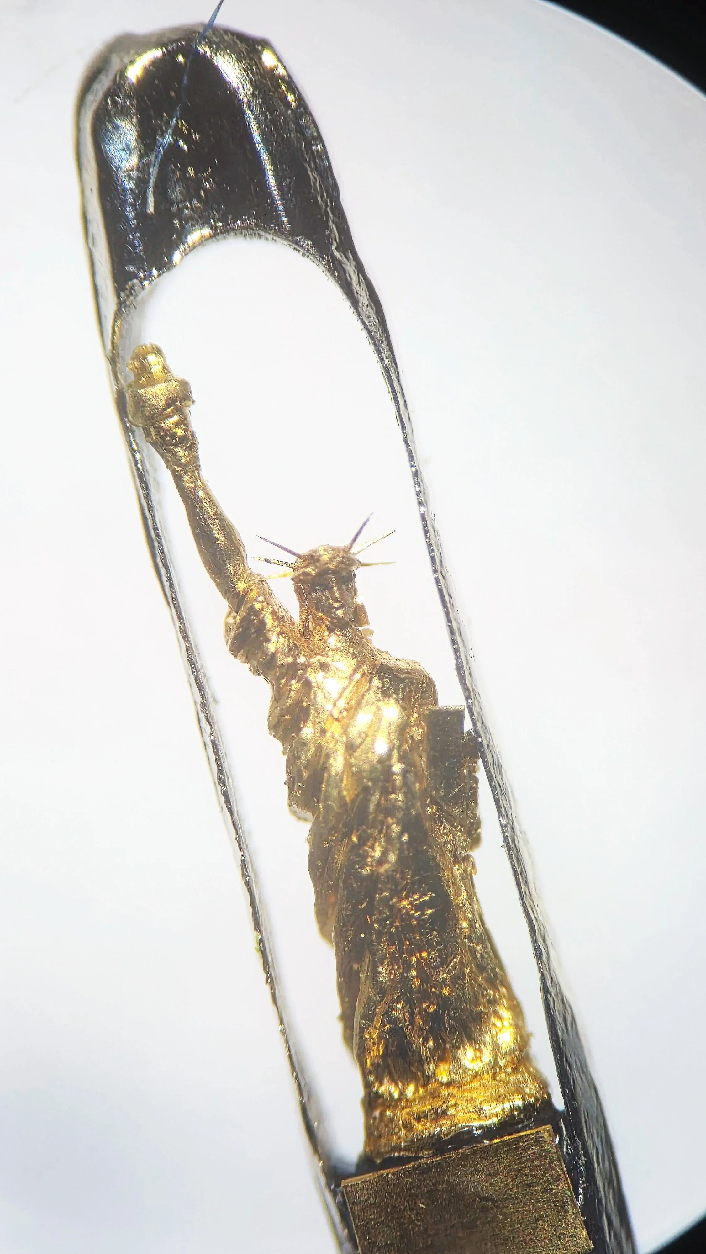 Close-up / Microscope View of the Sculpture 22 carat gold Statue of Liberty micro sculpture by Dr Willard Wigan MBE viewed through microscope, housed within the eye of a needle