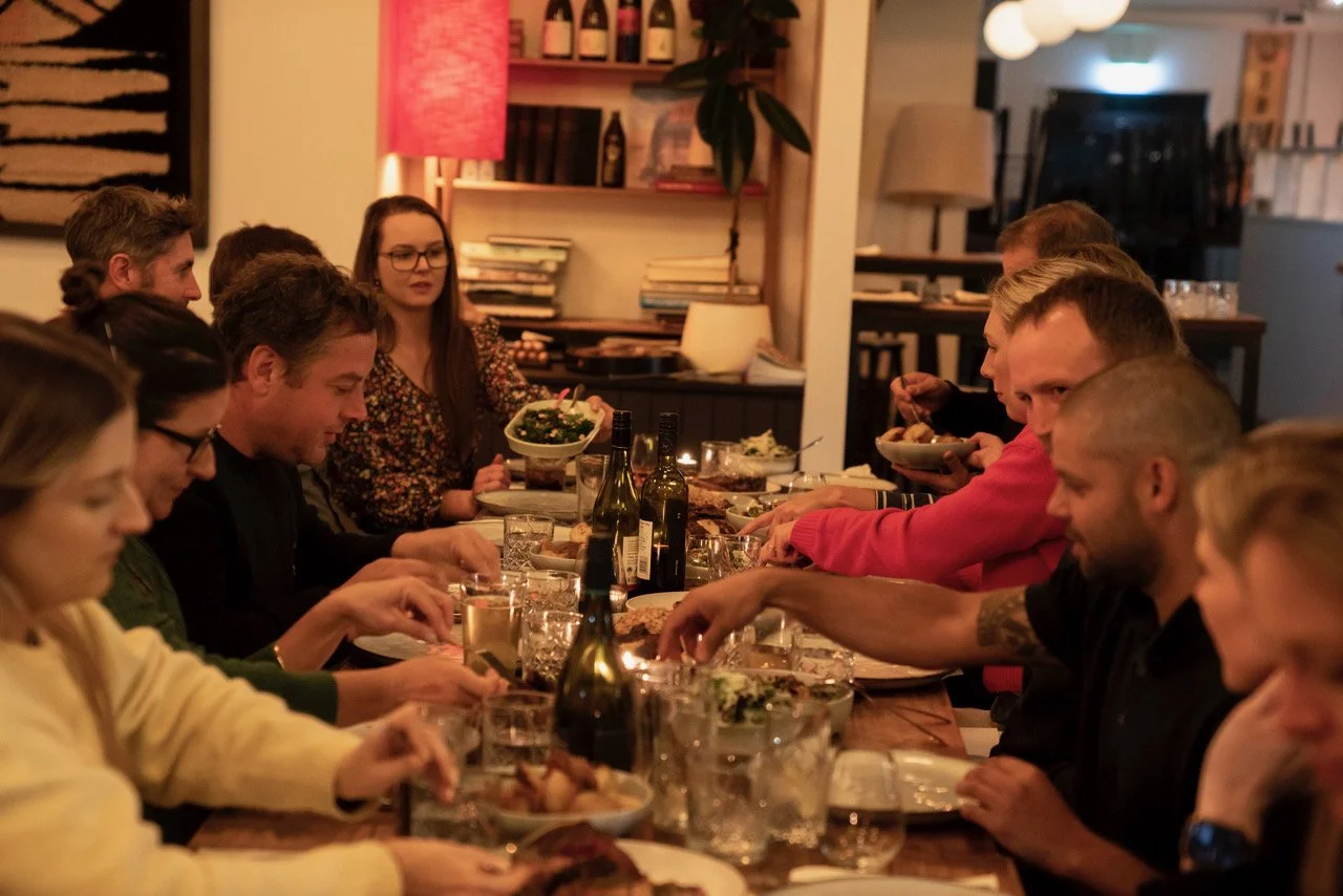 Family and friends gathered around a dining table enjoying a meal together at night in a warmly lit room