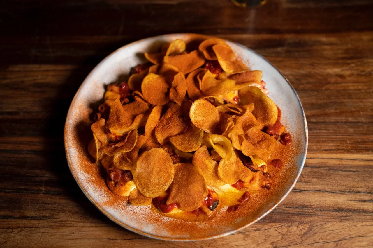 A plate of potato chips topped with ketchup on a wooden table.