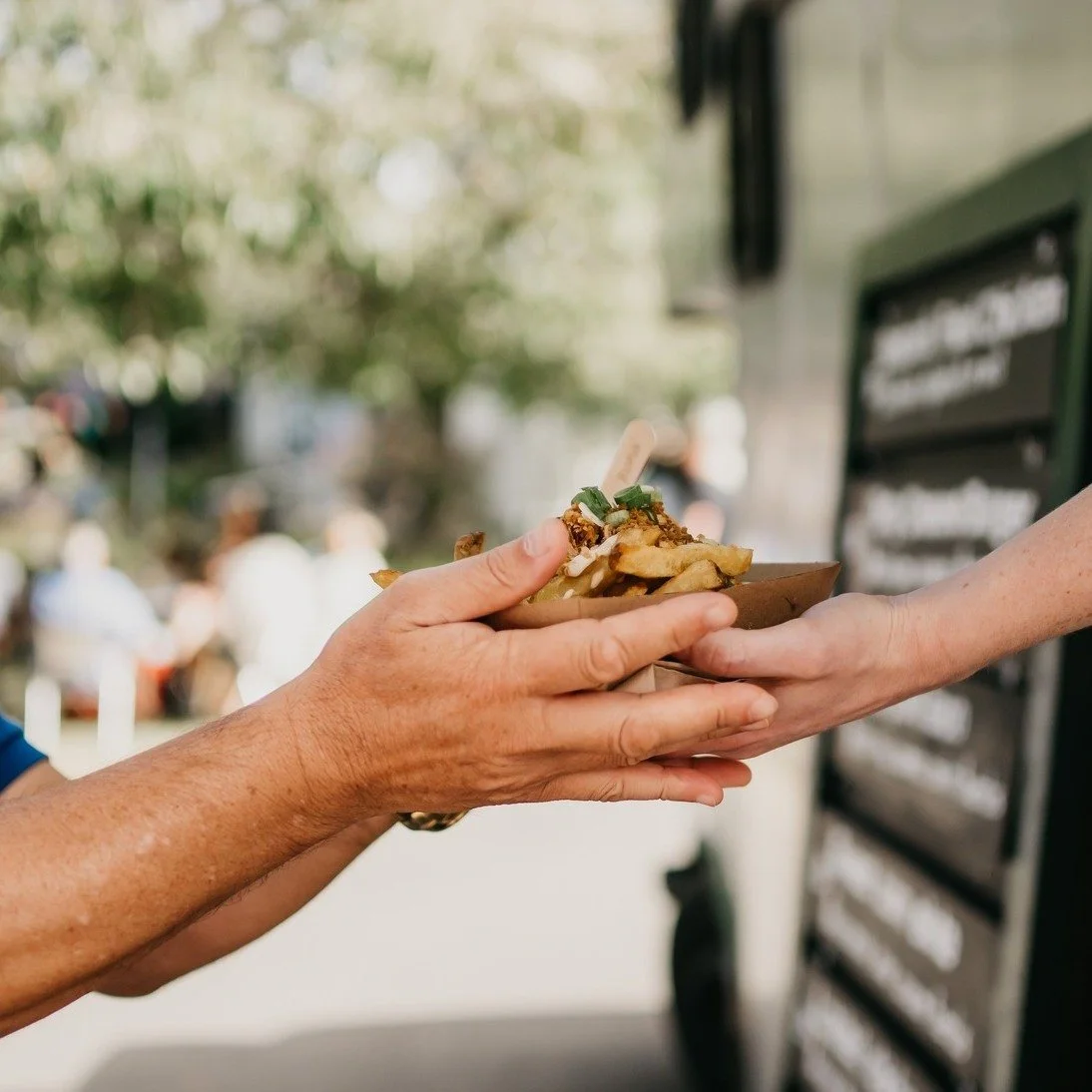 Person handing a paper tray with loaded fries to another person outside
