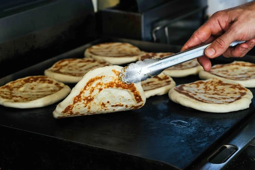 Person using tongs to handle a folded pancake on a griddle with other pancakes cooking.