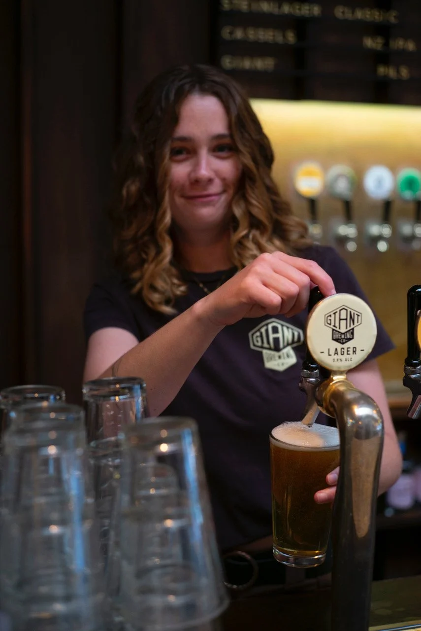 A woman is pouring a giant lager beer from a tap at a bar.