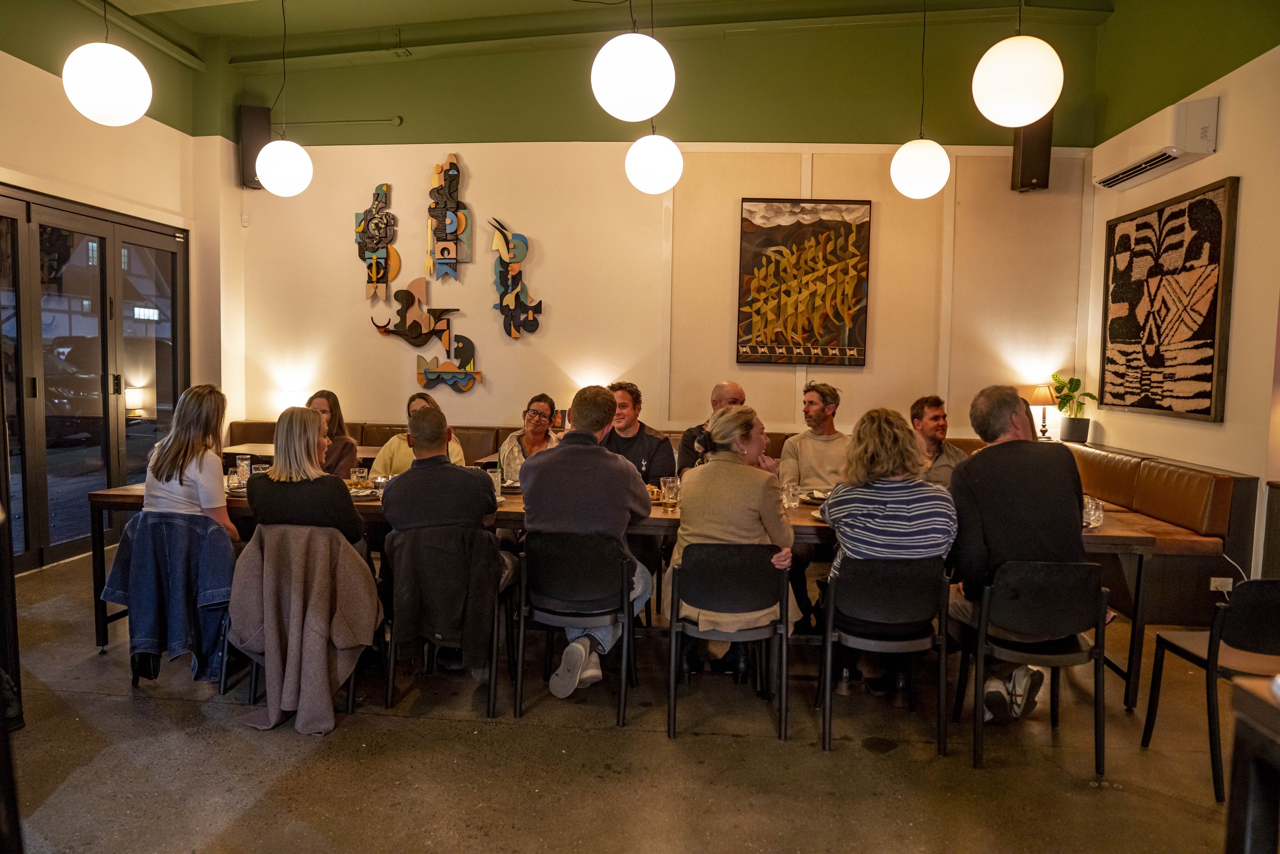 People sitting and socializing at a restaurant or cafe with modern art on the walls and warm lighting.