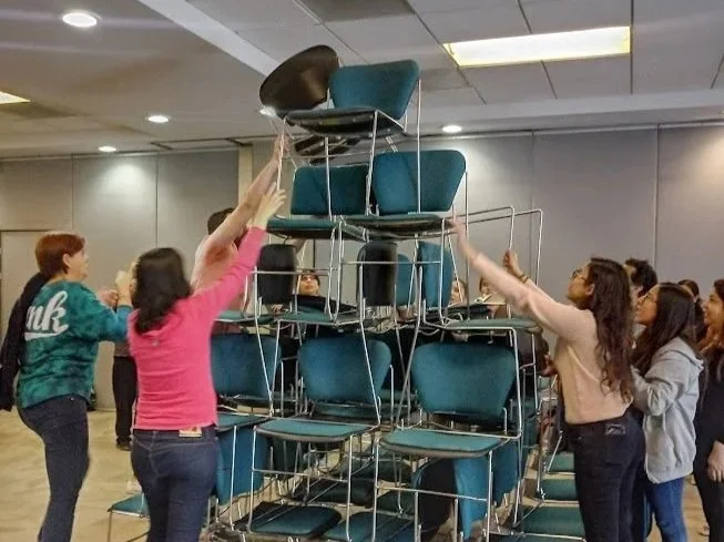 Niños construyendo una torre con sillas en una sala cerrada.