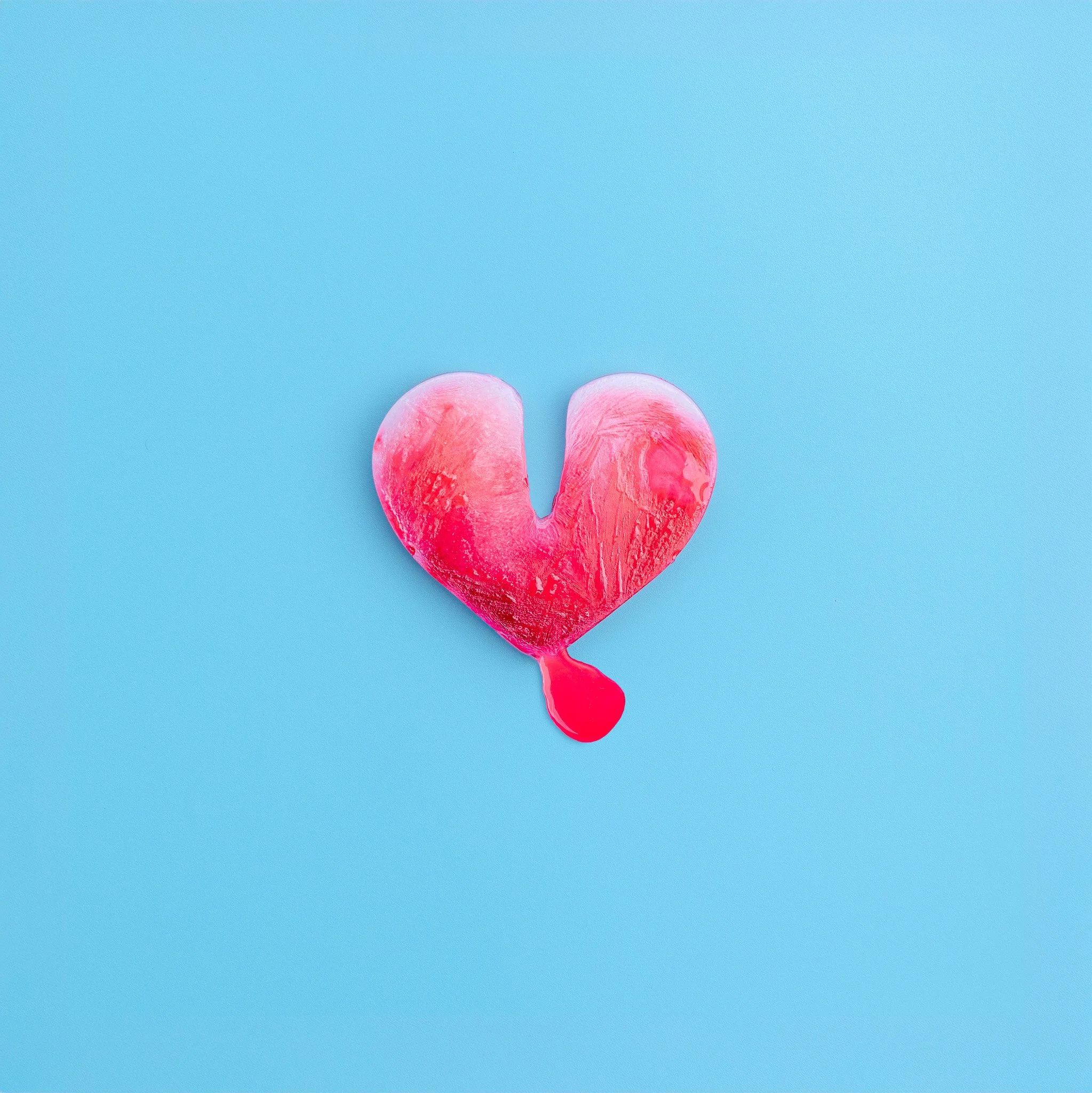 Close-up of a pink heart-shaped cotton candy with a small drip on a bright blue background.