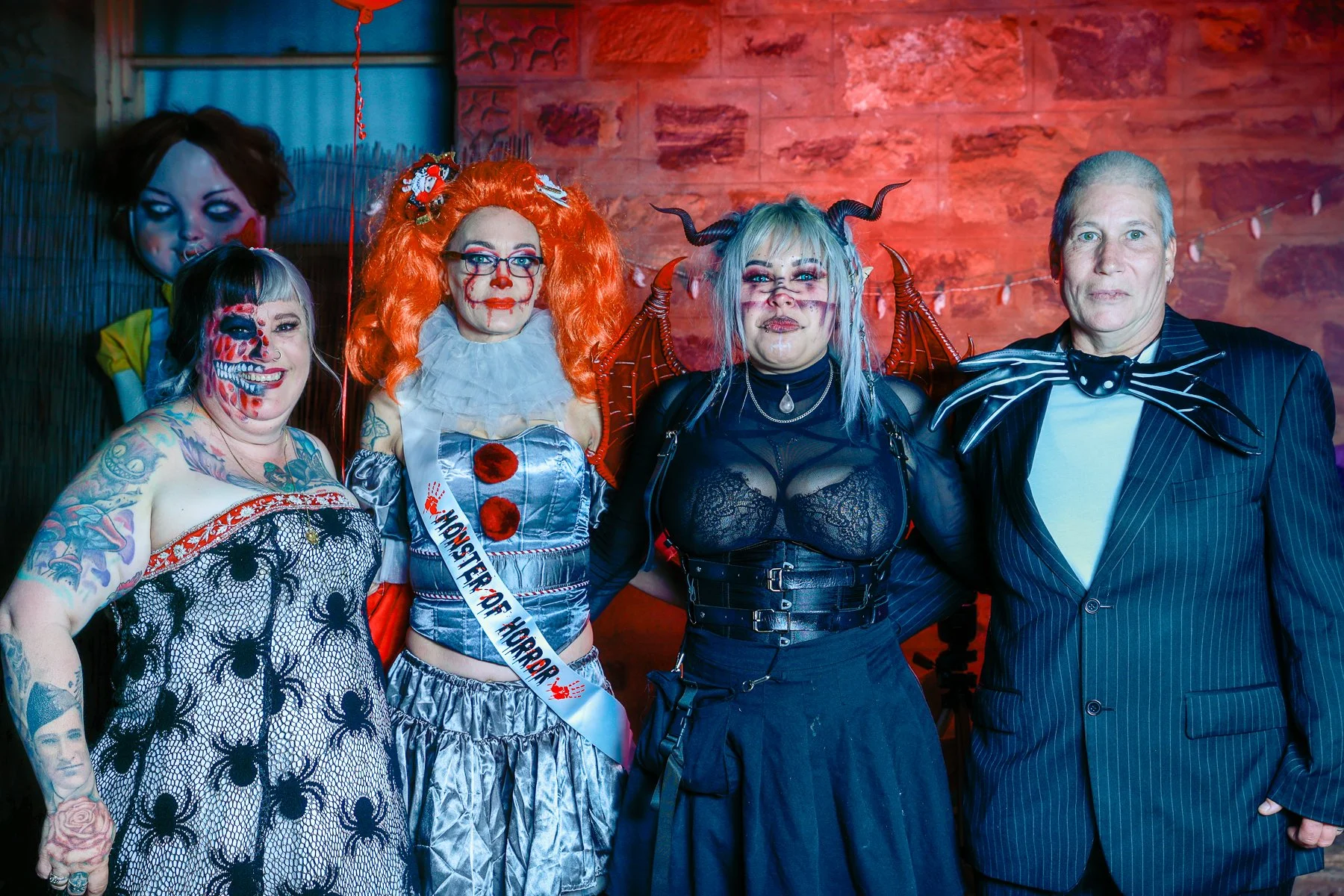 Group of people in Halloween costumes, including a clown, a vampire, and a character with a skull face.