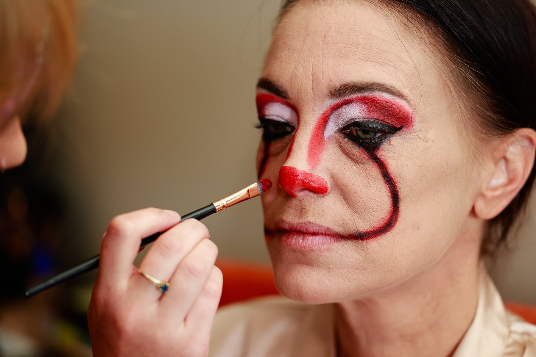 Person applying clown makeup on woman's face