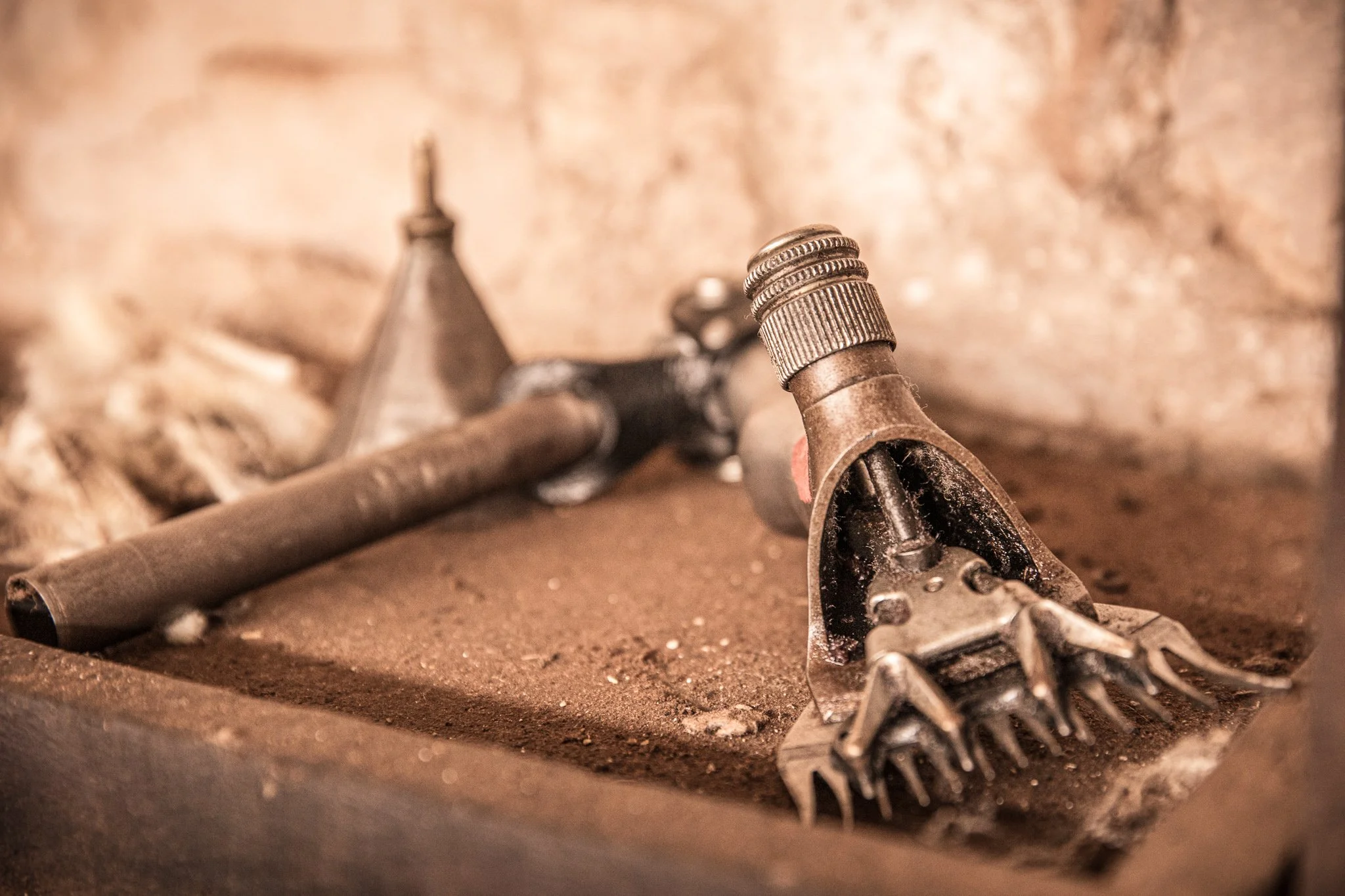Close-up of a shearing handpiece with a comb on a dusty workbench.