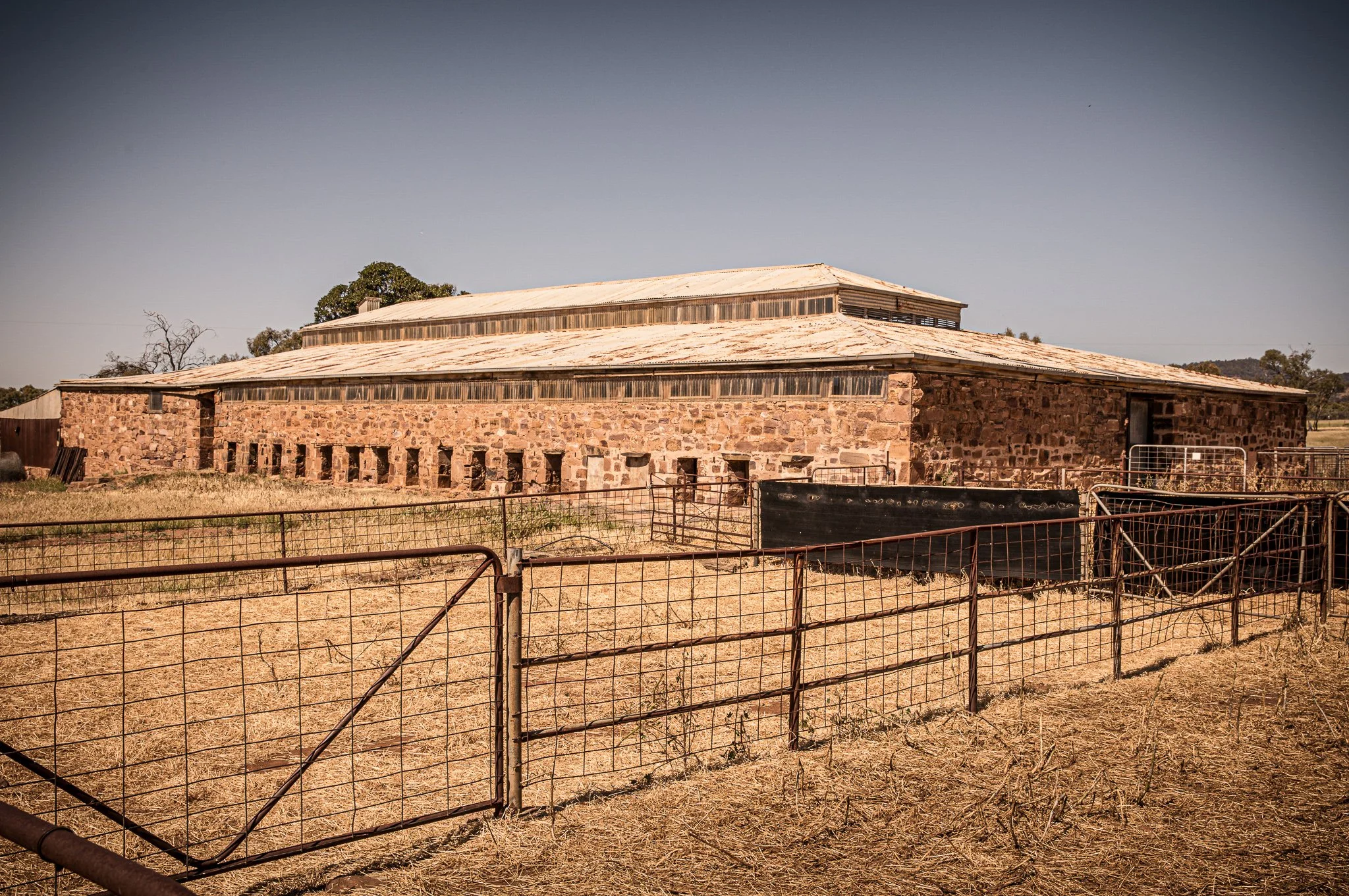 Stone farm building with metal roof and fenced yard