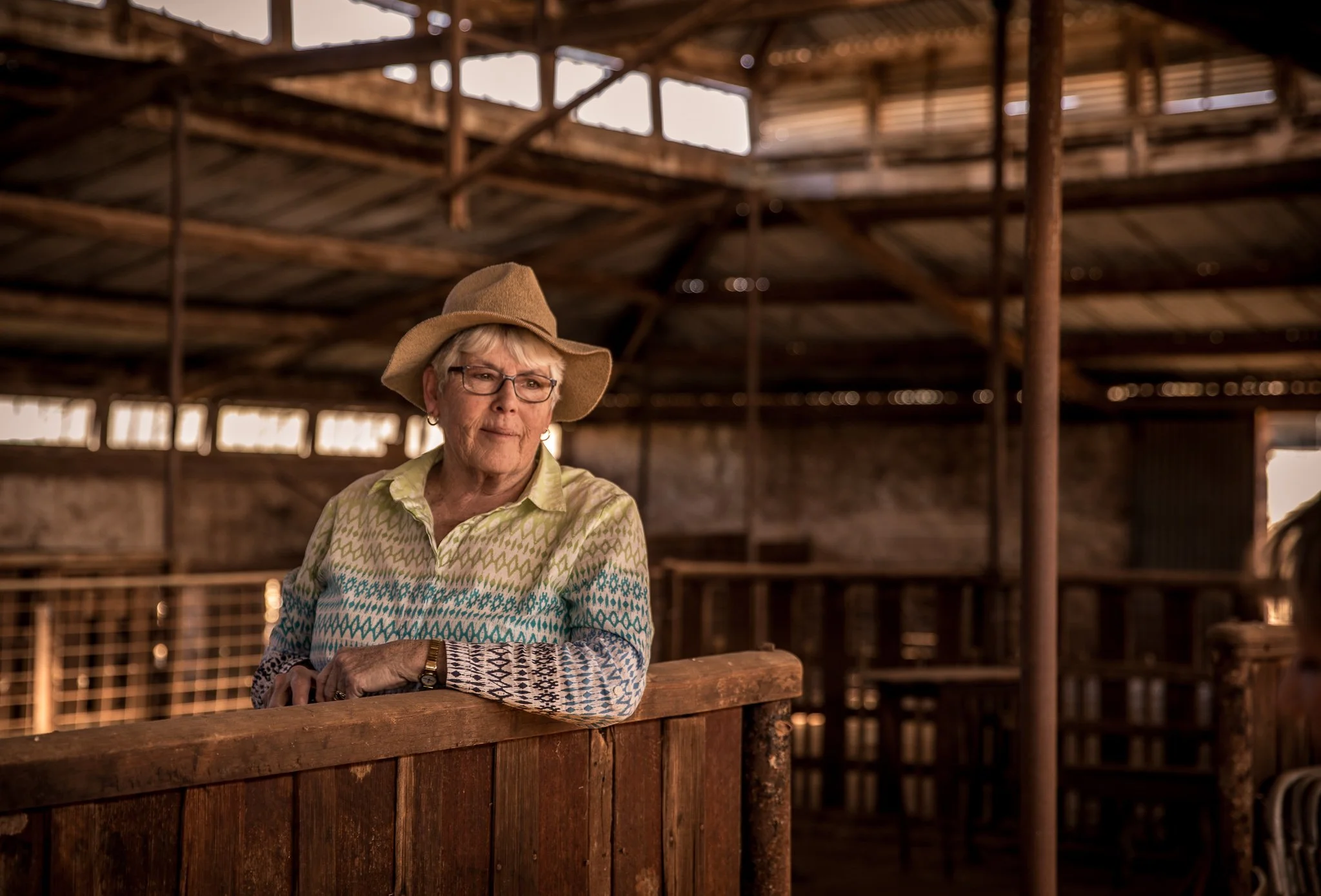 Elderly woman in a hat standing inside a rustic barn.