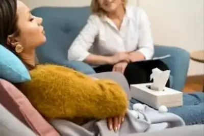 An image of a therapist undertaking RTT therapy sitting across from a client who is reclining in a chair, calm and quiet with eyes closed