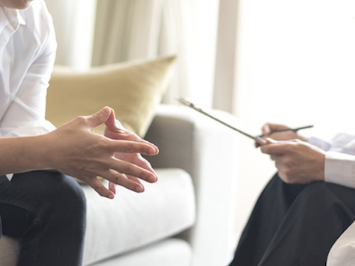 A close up image of 2 people undertaking outpatient rehab, they are sitting across from each other engaged in conversation and session