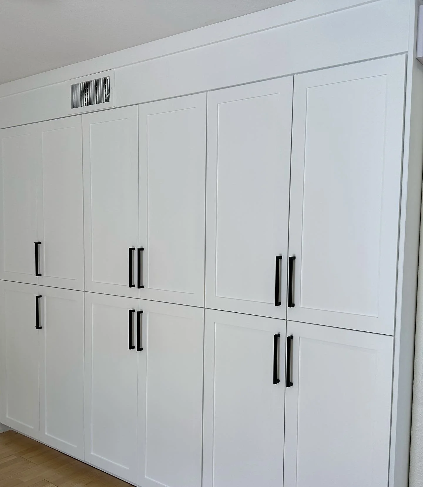 White built-in cabinet with black handles and an air vent on top.