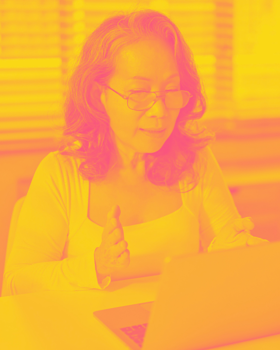 A trans Asian woman with glasses and curly hair looking at a laptop screen with a focused expression.