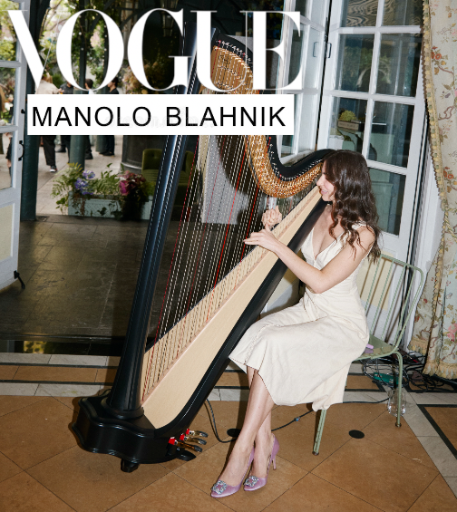 A woman in a white dress sitting on a chair, playing a large harp at a Vogue event featuring Manolo Blahnik.