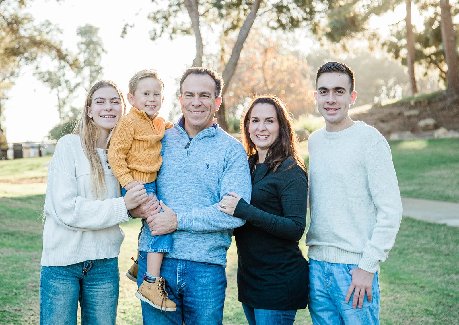 Family laughing and smiling while posing for a family photo at Tewinkle Park in Costa Mesa, CA