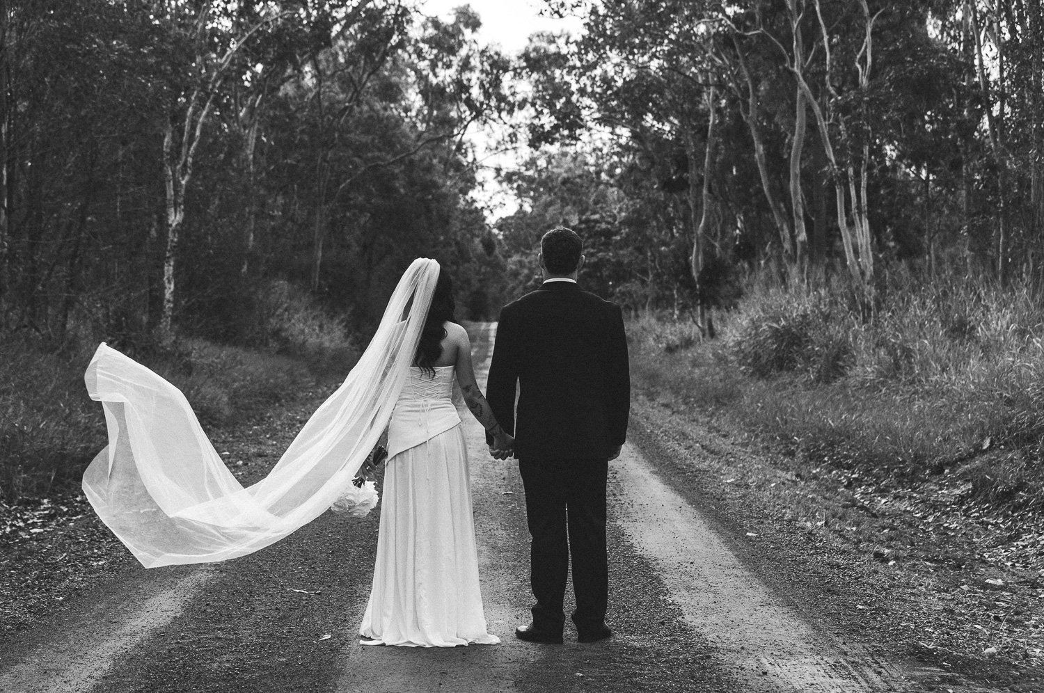 Bride and groom walking down road with veil blowing