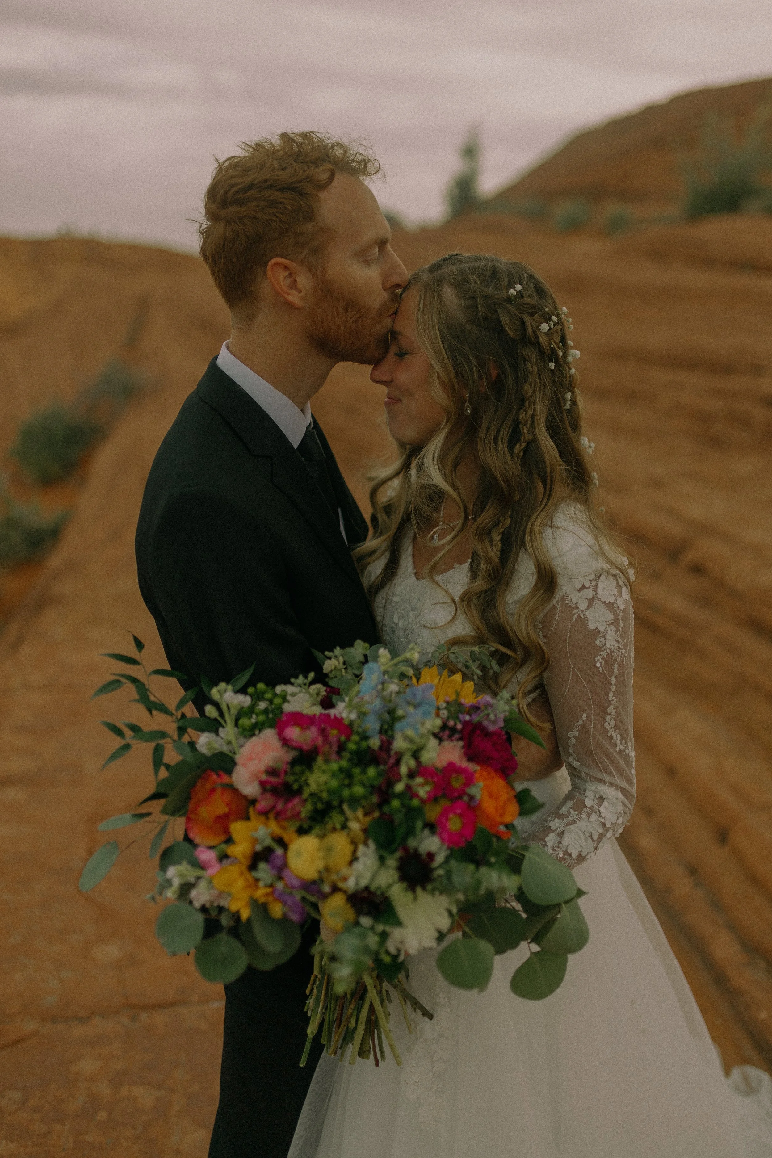 Bride and groom embracing at desert wedding with colorful bouquet.