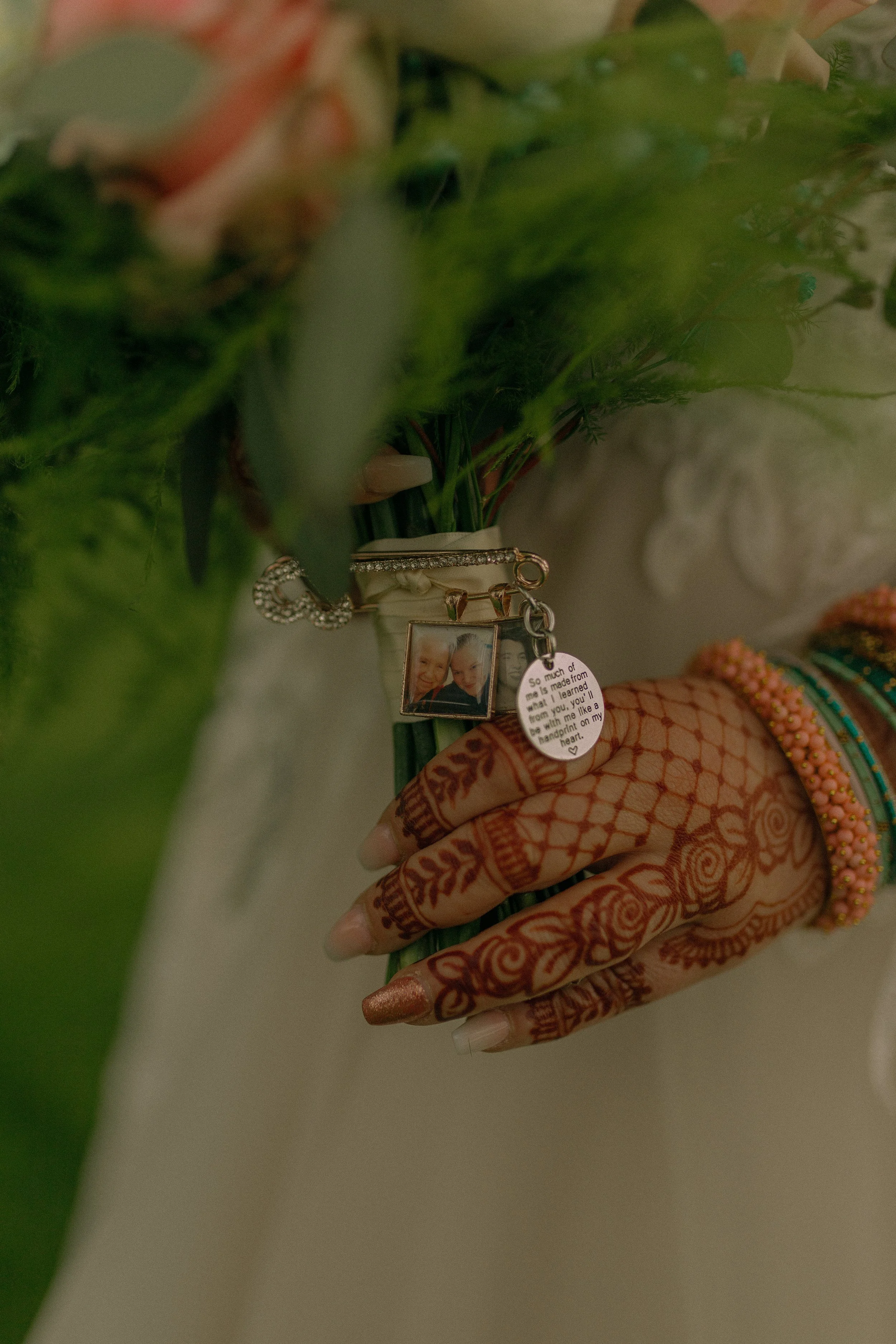 Close-up of a henna-decorated hand holding a bouquet wrapped with sentimental charms and photos.