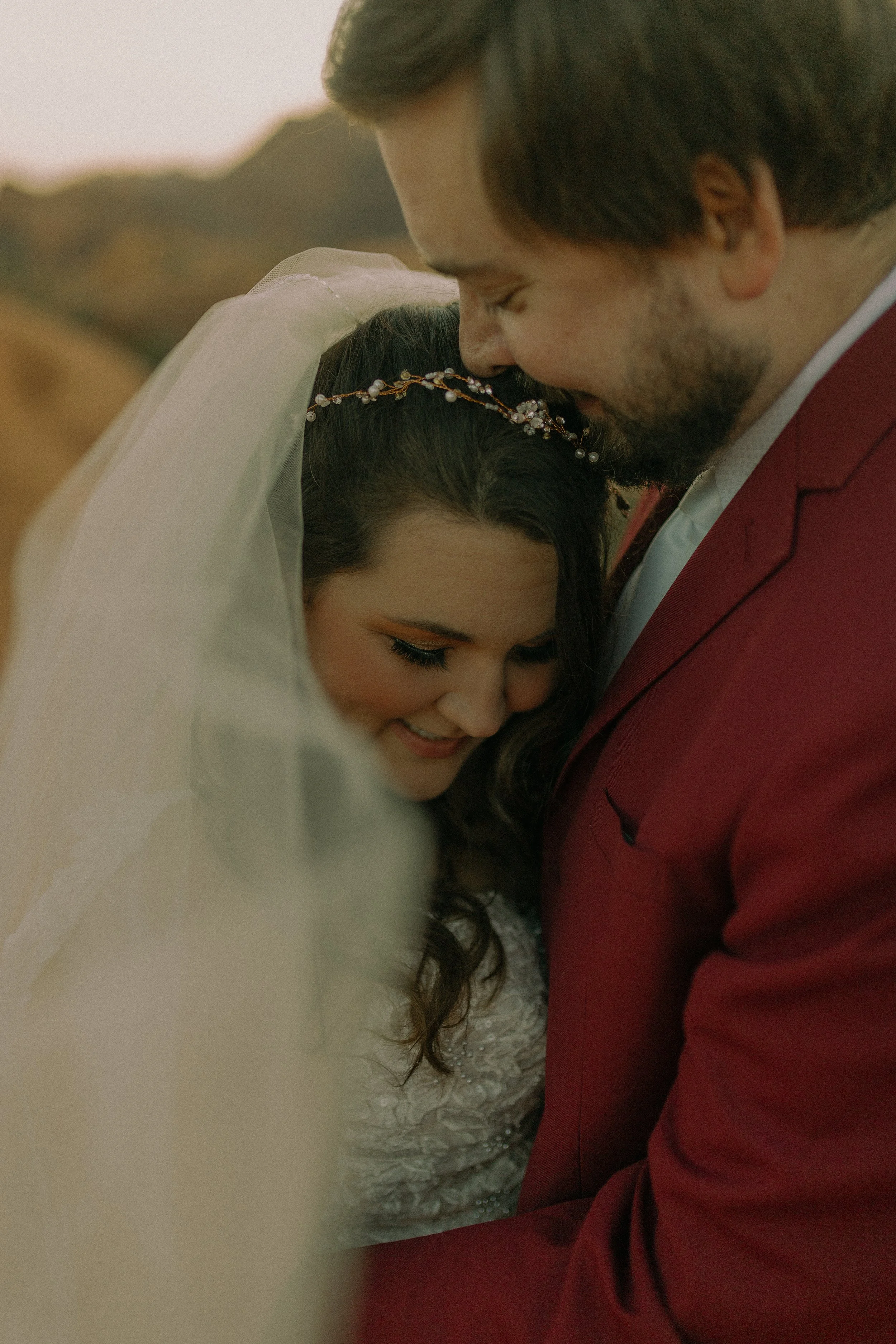 Bride and groom embracing with veil, softly lit in outdoor setting.