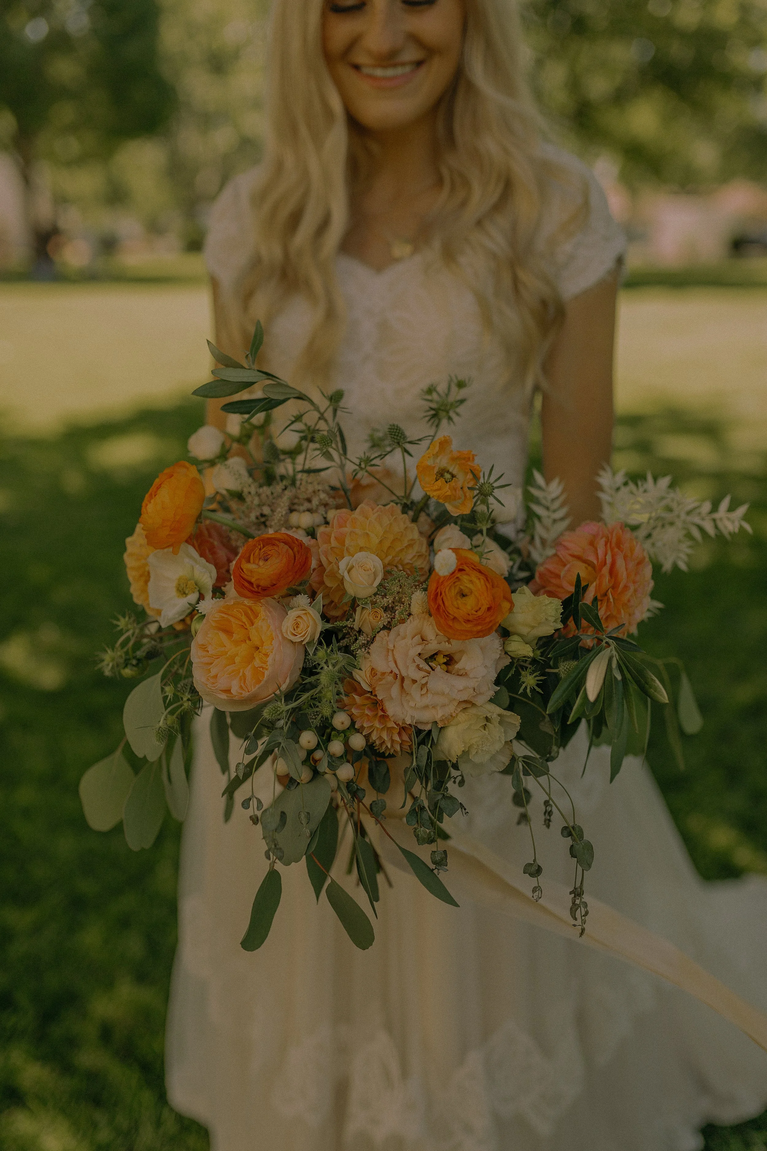 Bride holding a bouquet of orange and pink flowers in a garden setting.