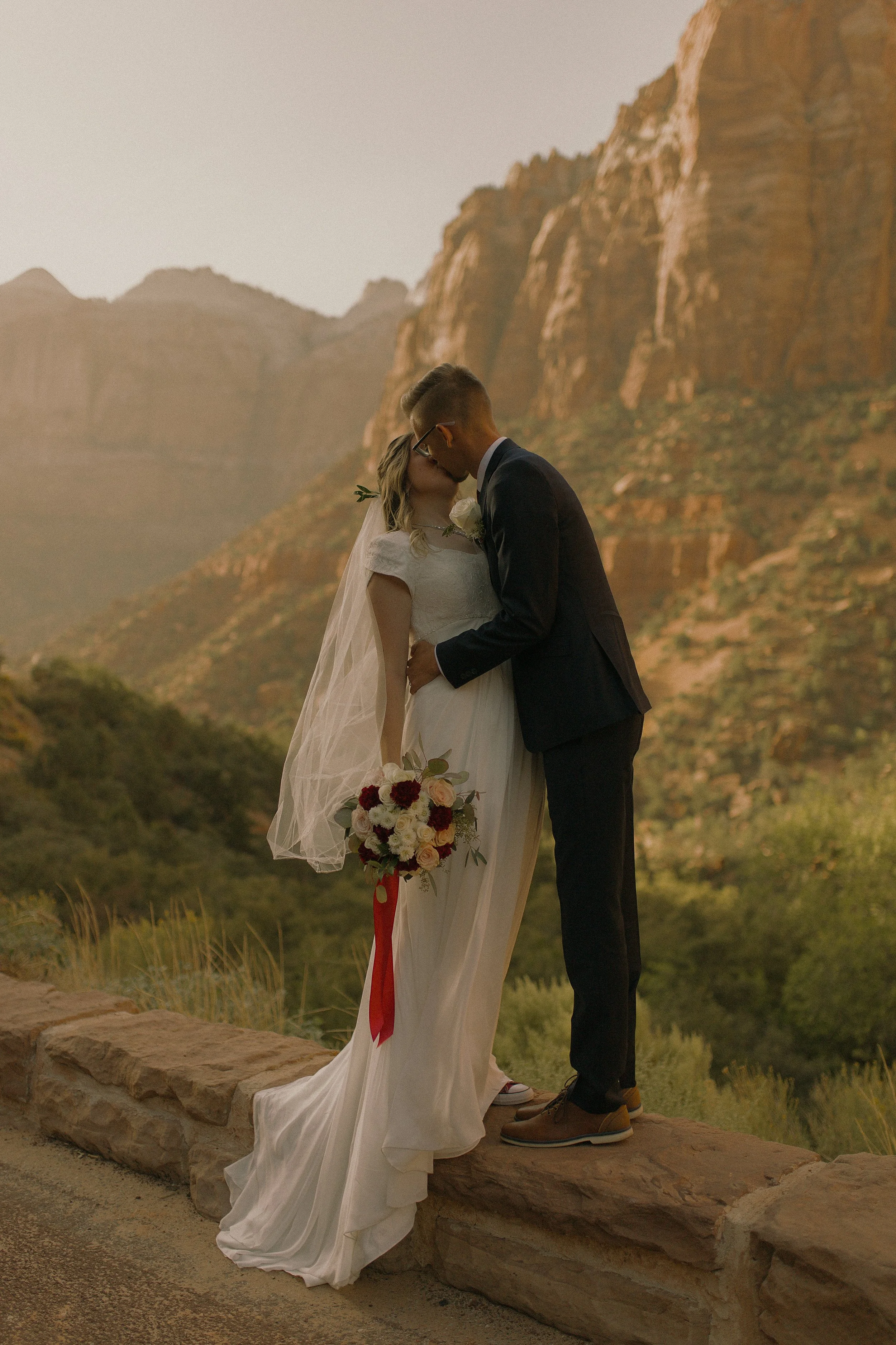 Bride and groom kissing at a scenic overlook with red rock cliffs in the background.
