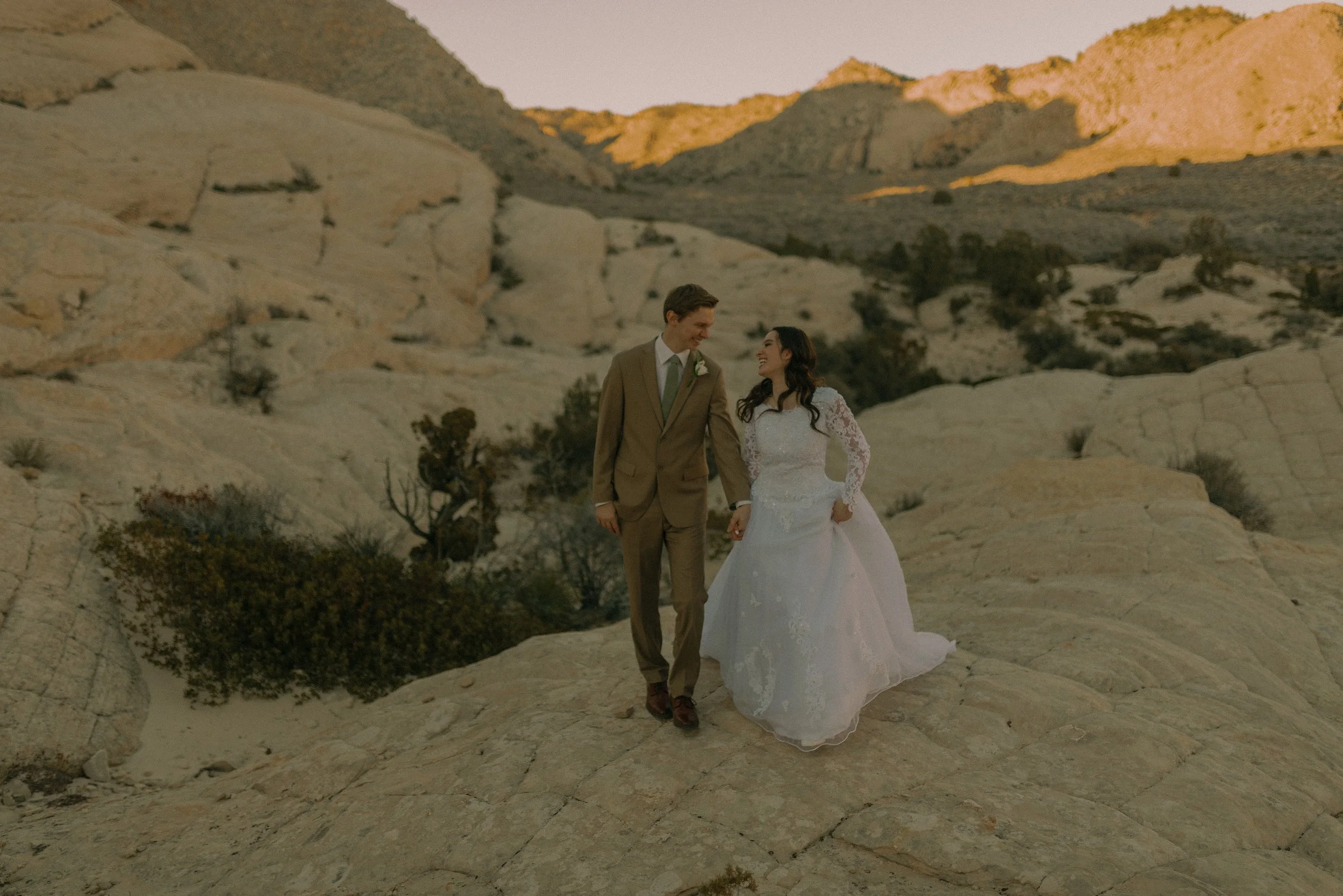 Bride and groom walking on rocky landscape with mountains in the background.